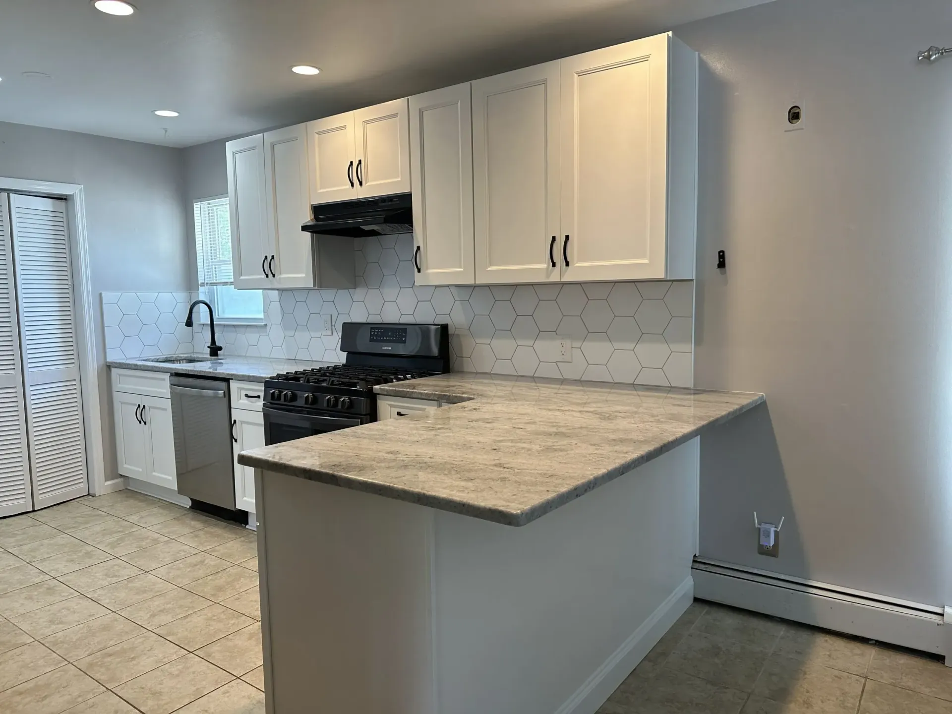Empty modern kitchen with white cabinets, gray countertops, stainless stove, and tiled floor