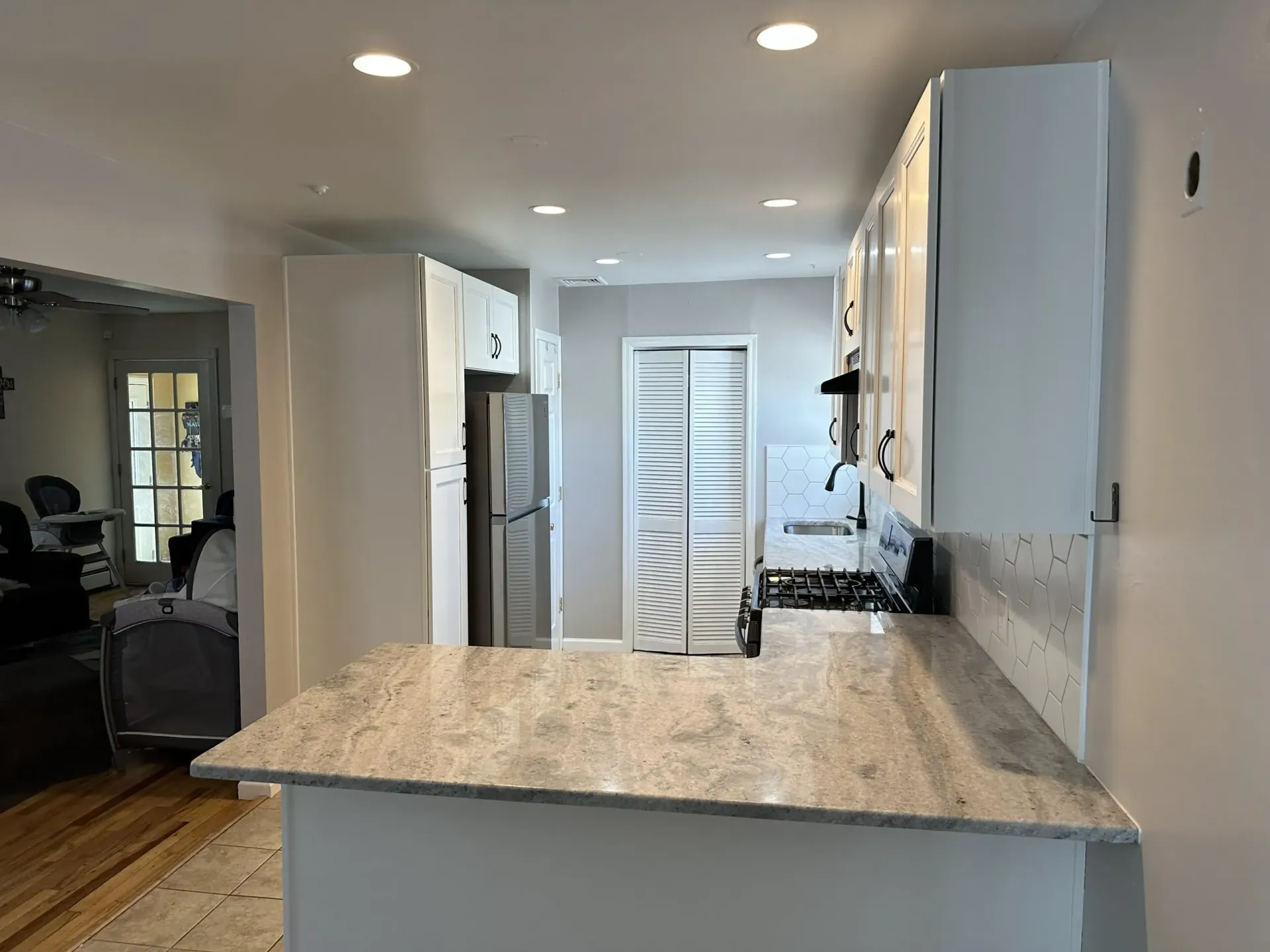 Bright kitchen with granite island, stainless fridge, white cabinets, and hardwood floors.