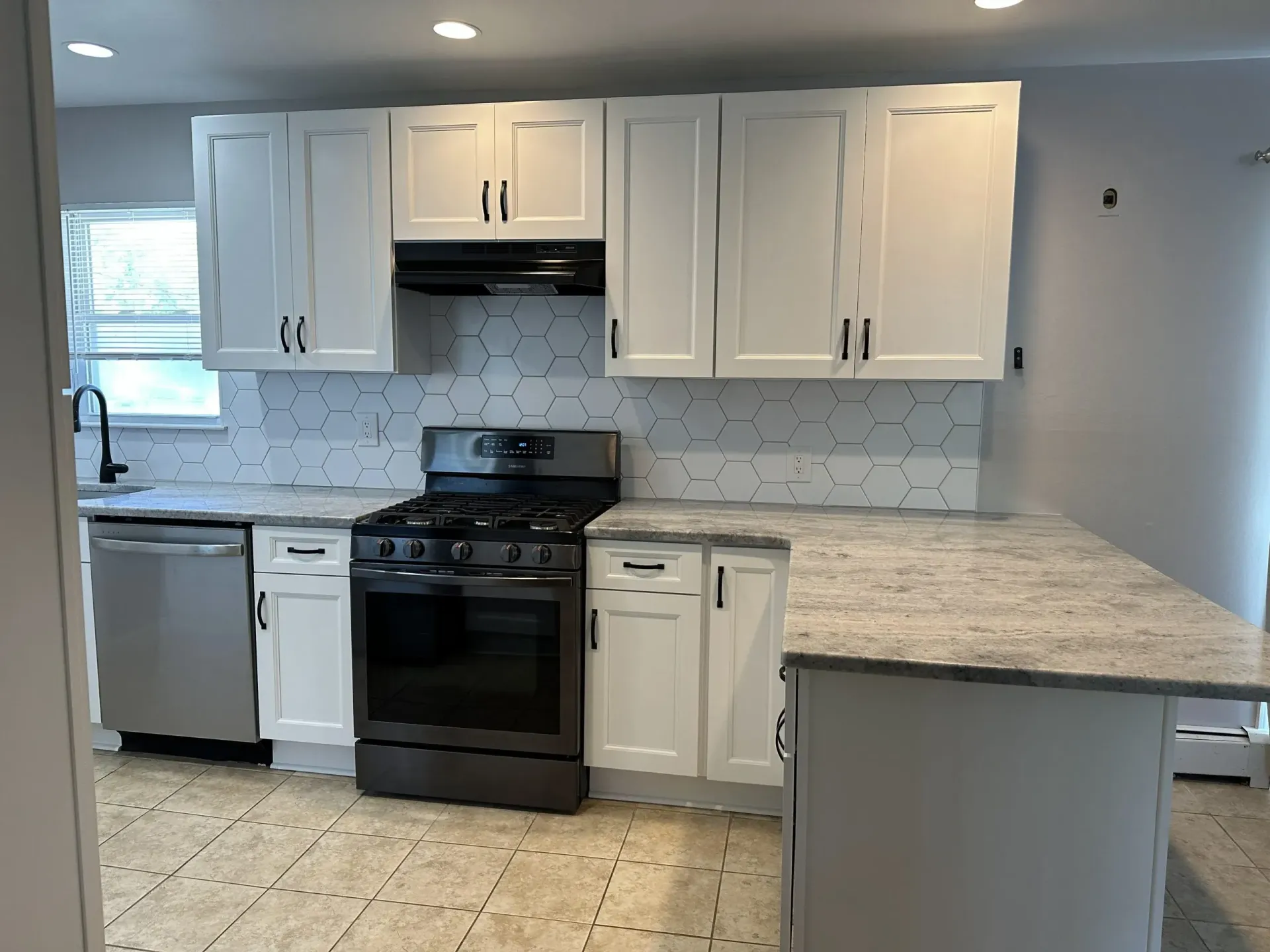 Empty kitchen with white cabinets, black stove, granite countertops, and stainless dishwasher.
