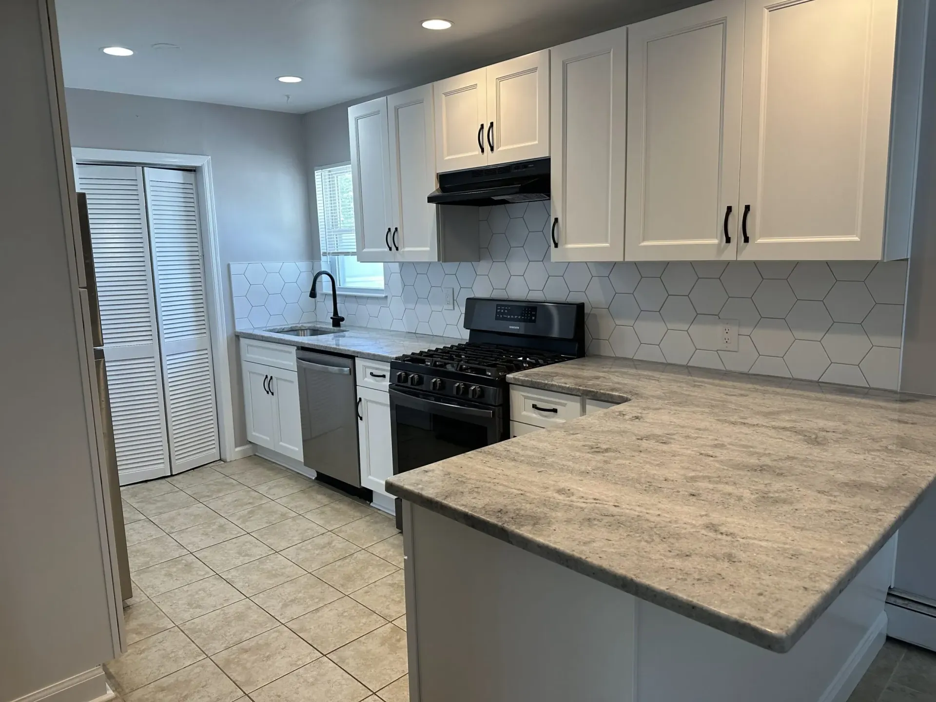 Bright kitchen with white cabinets, stainless stove, beige counters, and tiled floor