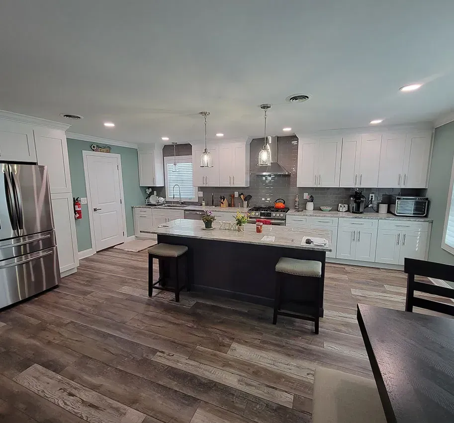 Modern kitchen with white cabinets, gray island, stainless fridge, and wood floors