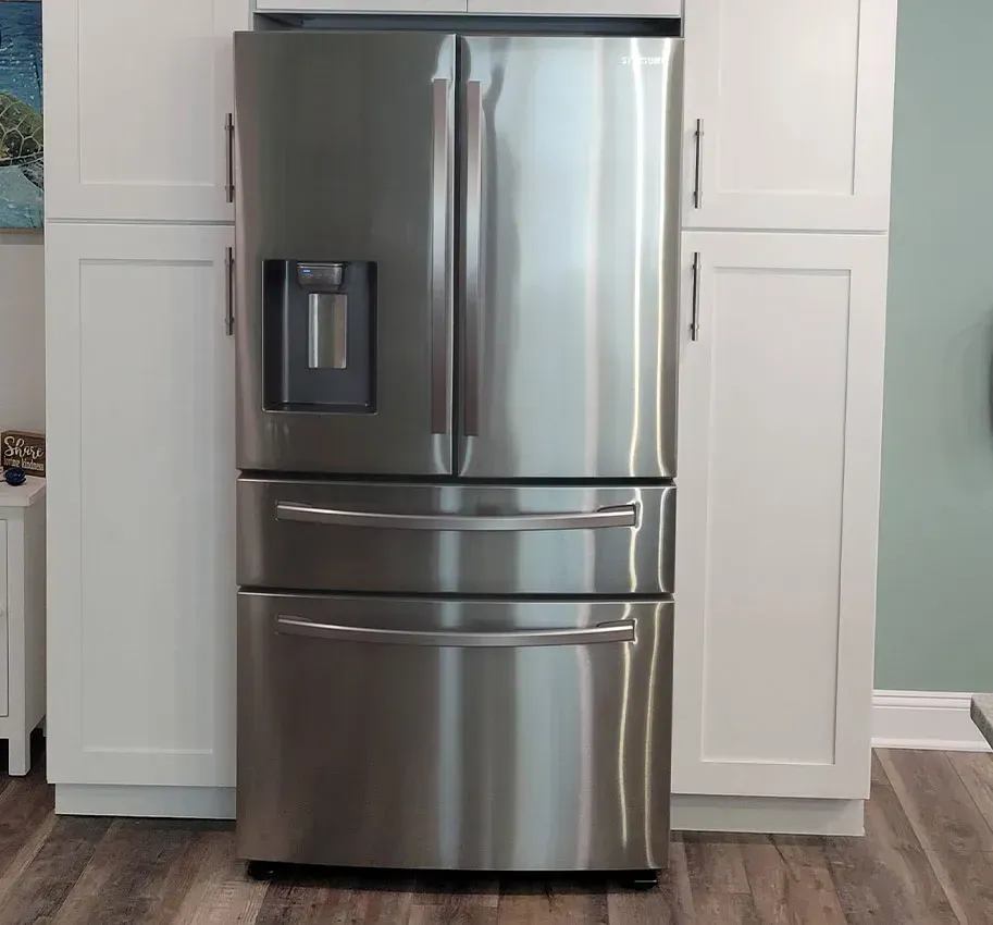 Stainless steel French-door refrigerator with water dispenser, built into white kitchen cabinetry.