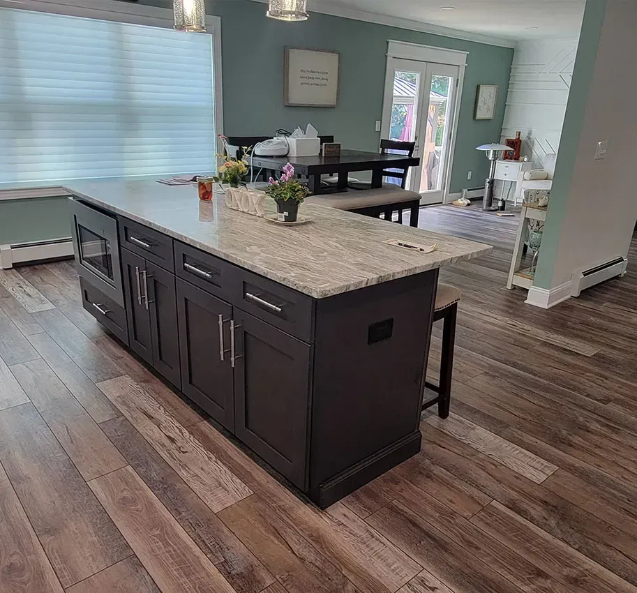 Modern kitchen with dark island cabinets, light countertops, wood floors, and an open dining area.