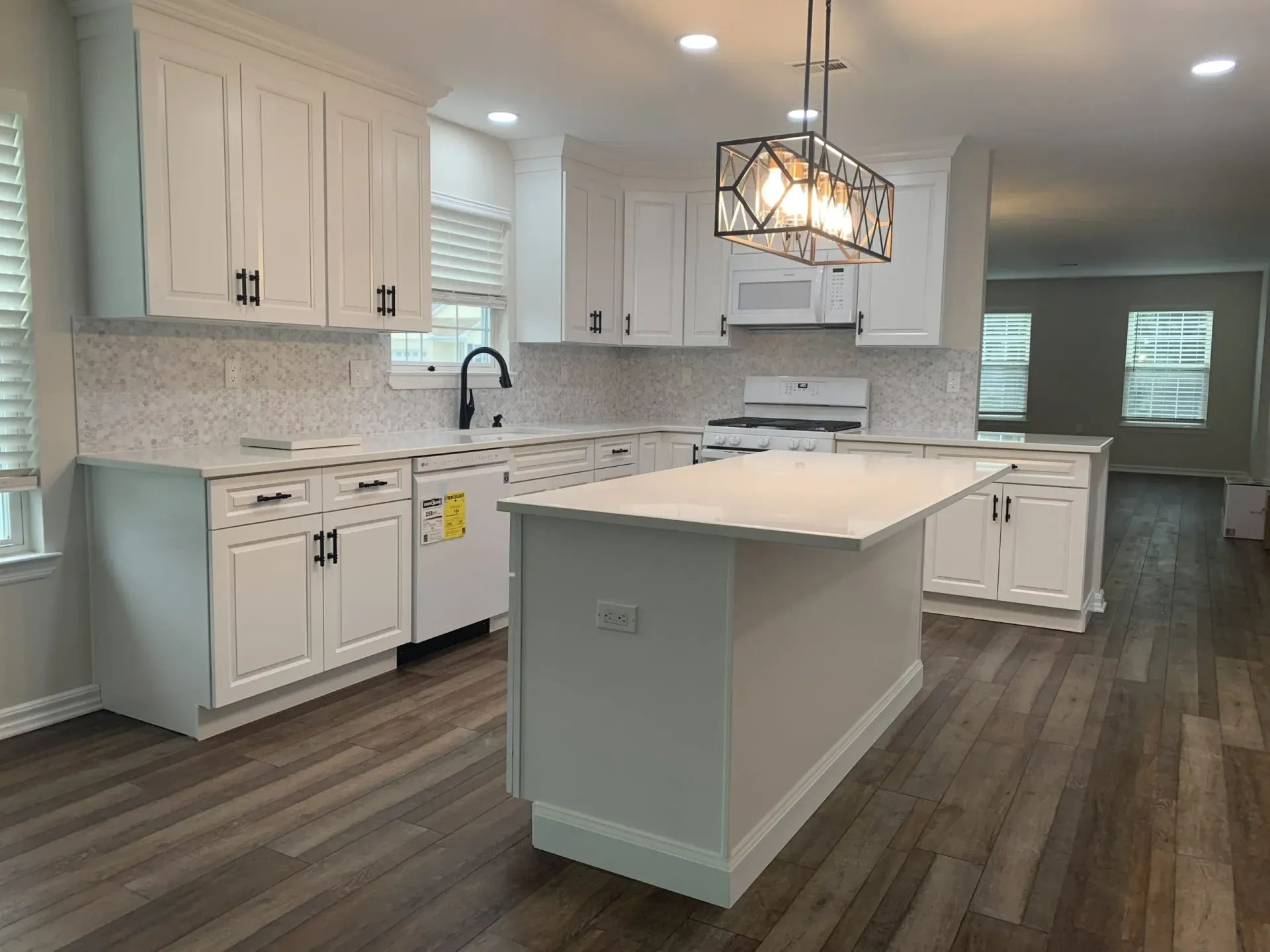 Bright white kitchen with a large island, pendant light, and dark wood floors