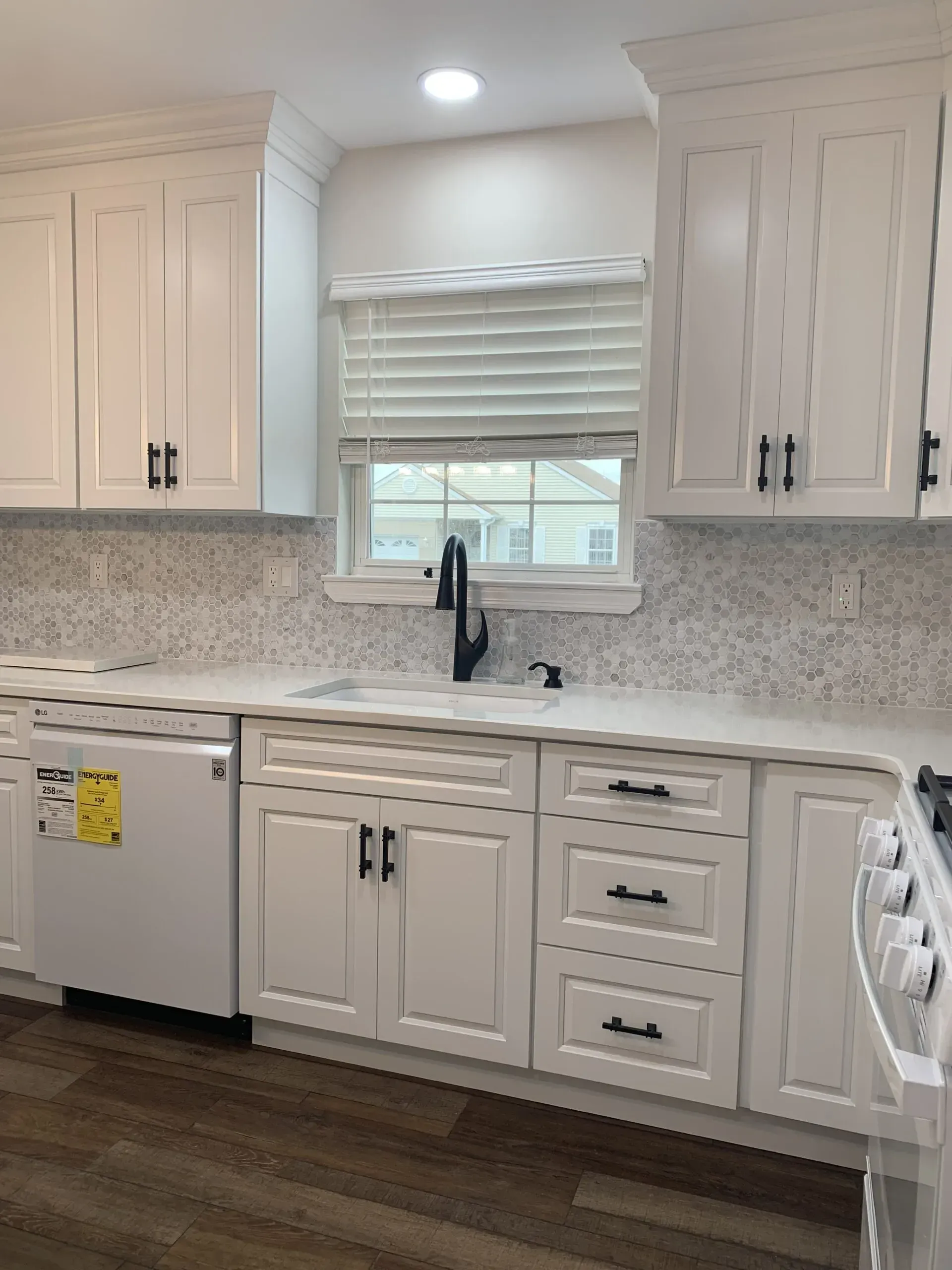 Modern kitchen with white cabinets, marble-look countertops, dark wood floor, and a window over the sink