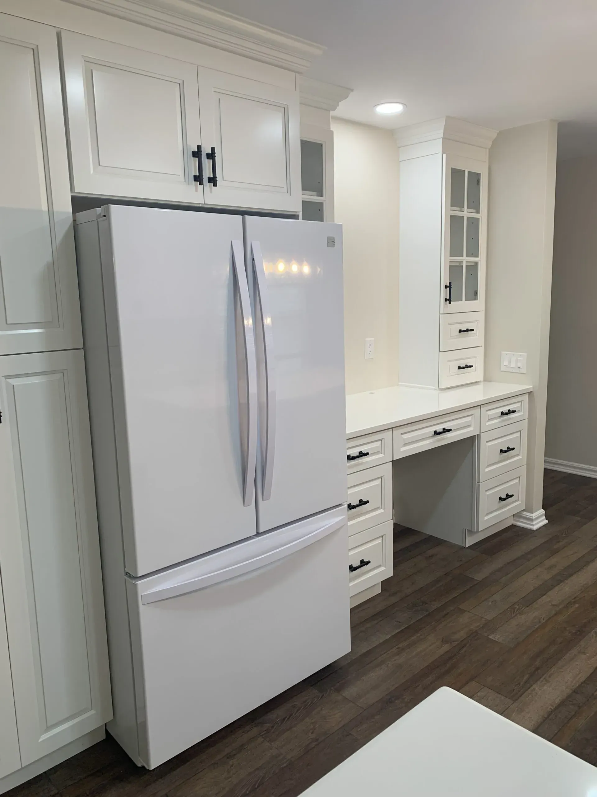White kitchen with a large refrigerator and built-in desk area against a wall.