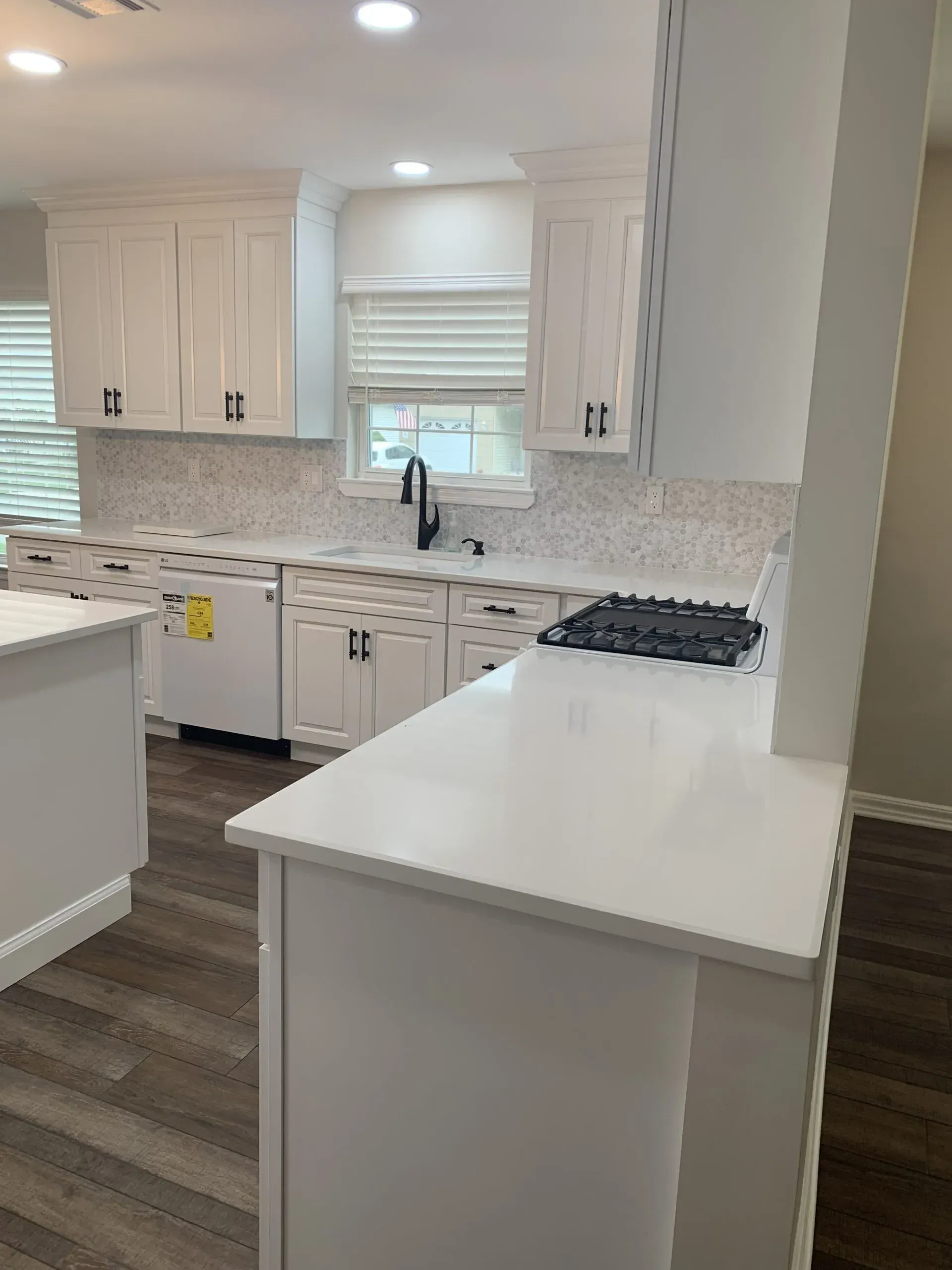 Bright white kitchen with island, white cabinets, mosaic backsplash, and dark wood flooring.