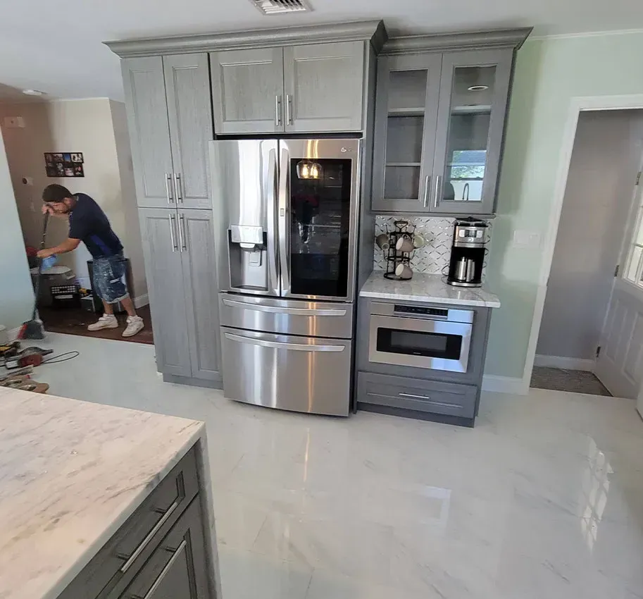 Modern kitchen with gray cabinetry, stainless steel appliances, and a person cleaning near the counter