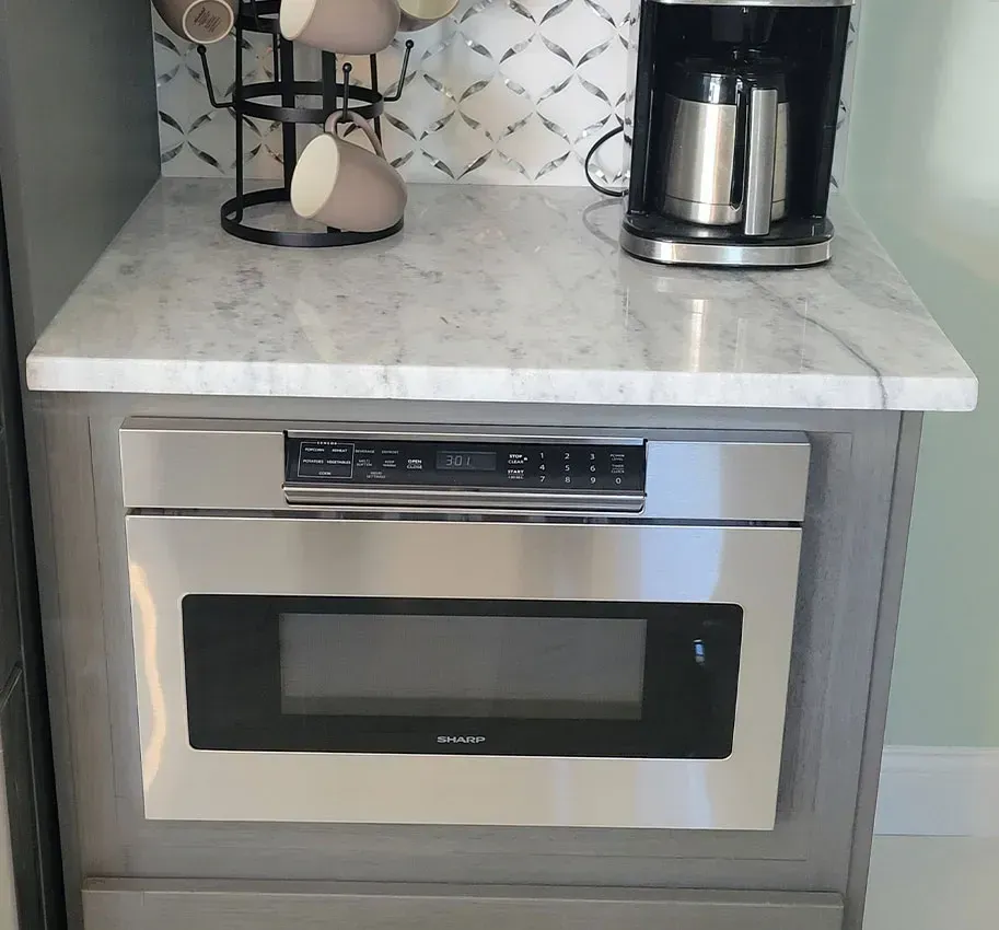 Built-in stainless steel microwave under a marble countertop with a coffee maker on top