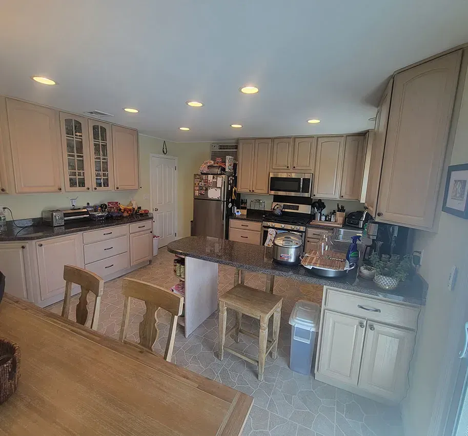 Bright kitchen with island, white cabinets, dining table, and recessed lights