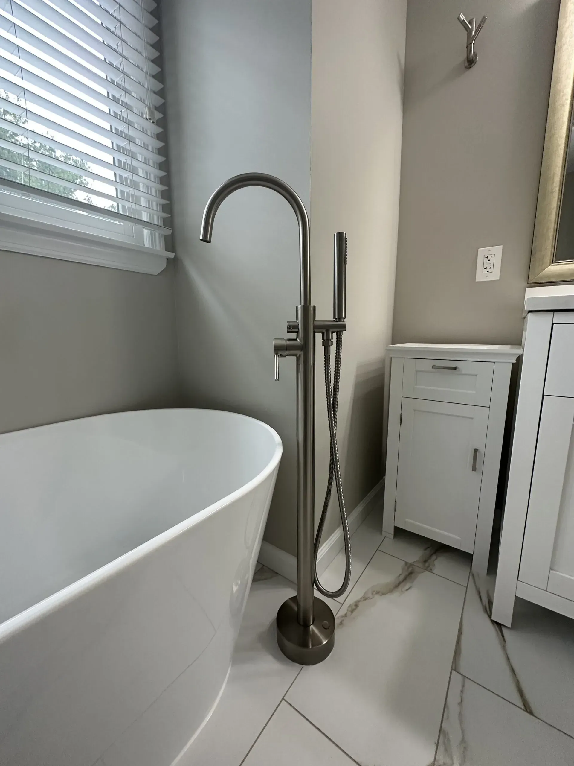 Modern bathroom with freestanding tub, chrome floor faucet, window blinds, and white vanity cabinet