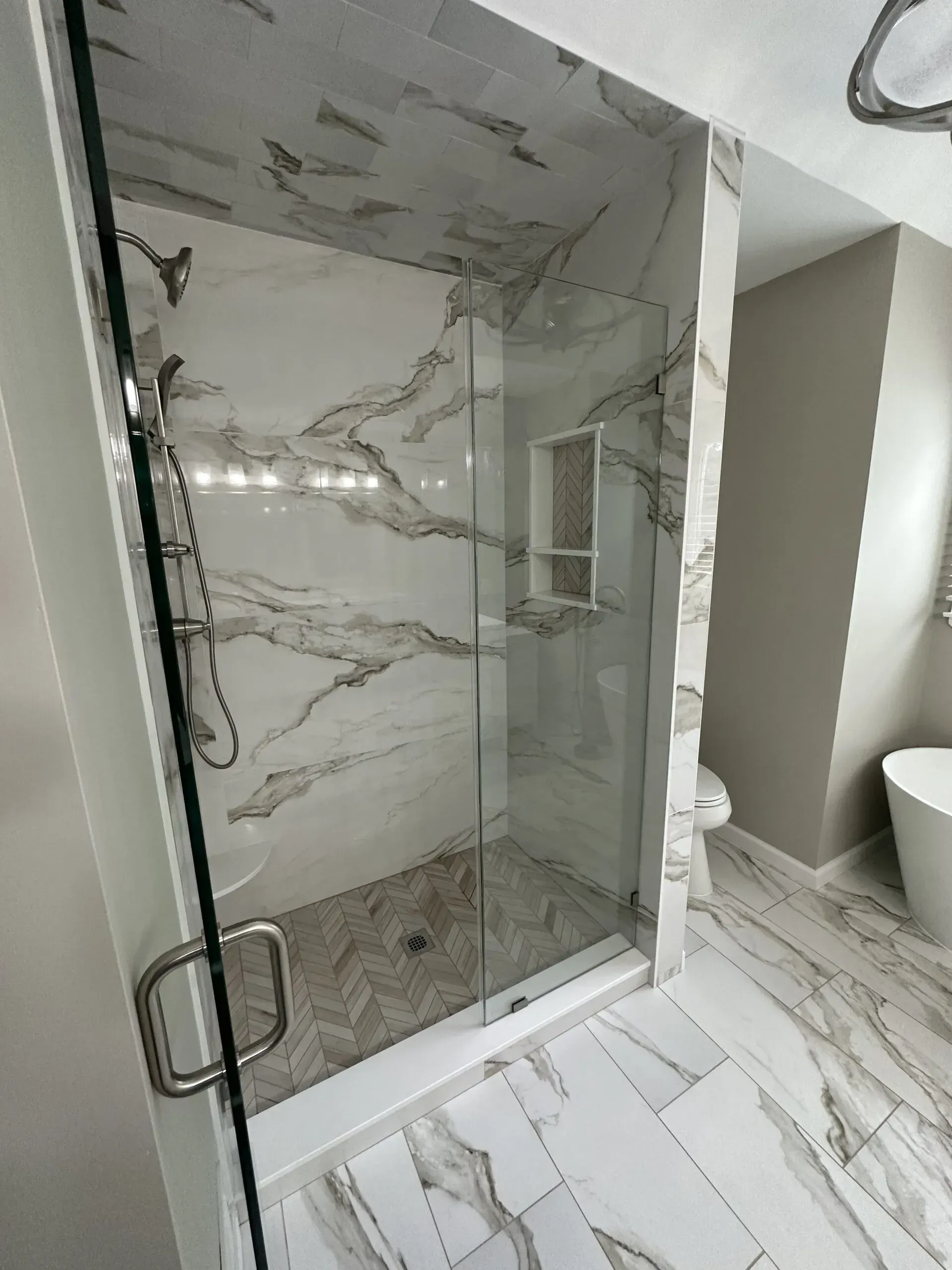 Glass-enclosed marble shower in a bright bathroom with white and gray tile