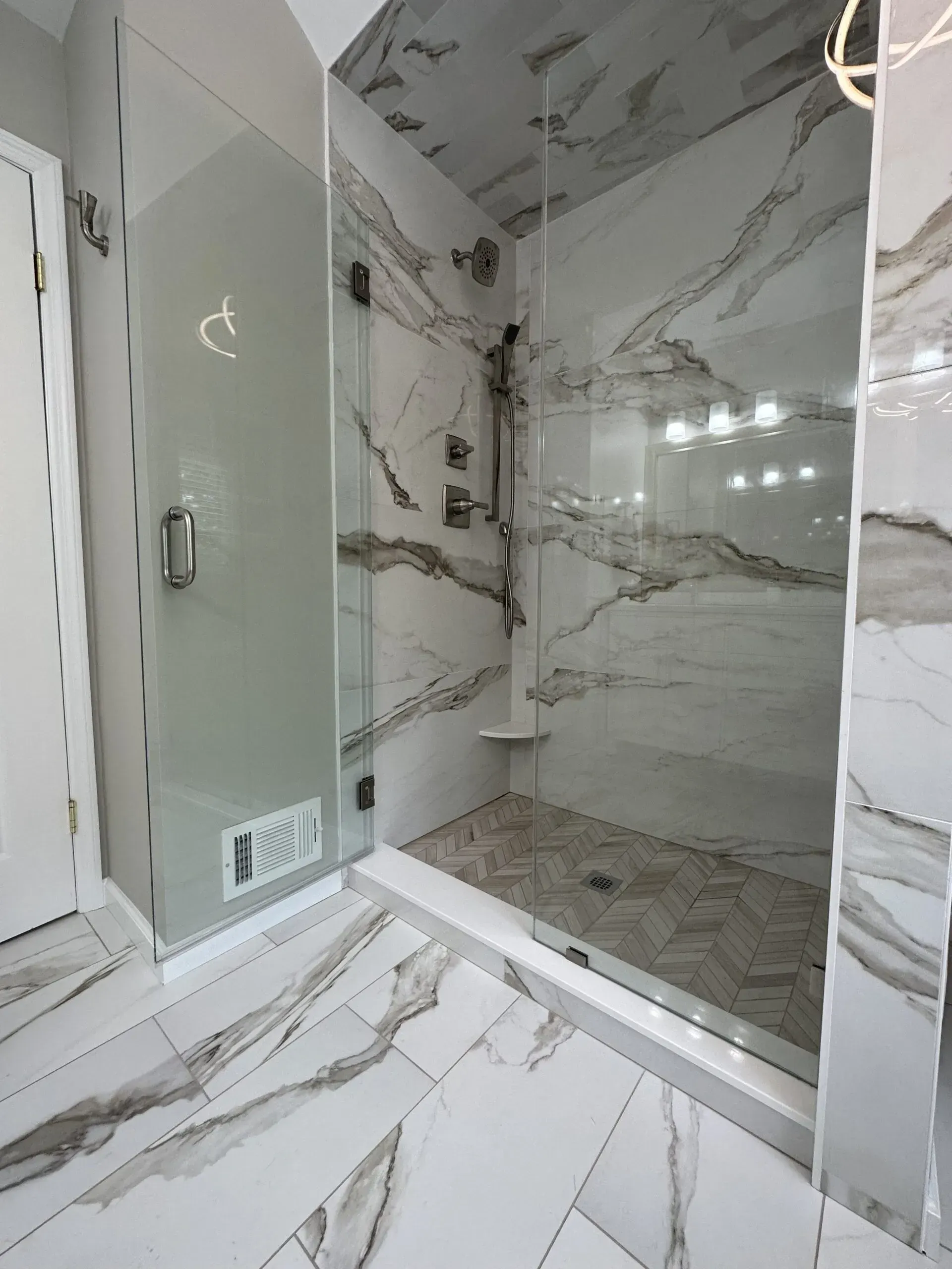 Modern marble-tile bathroom with a glass shower, vanity, and chrome fixtures