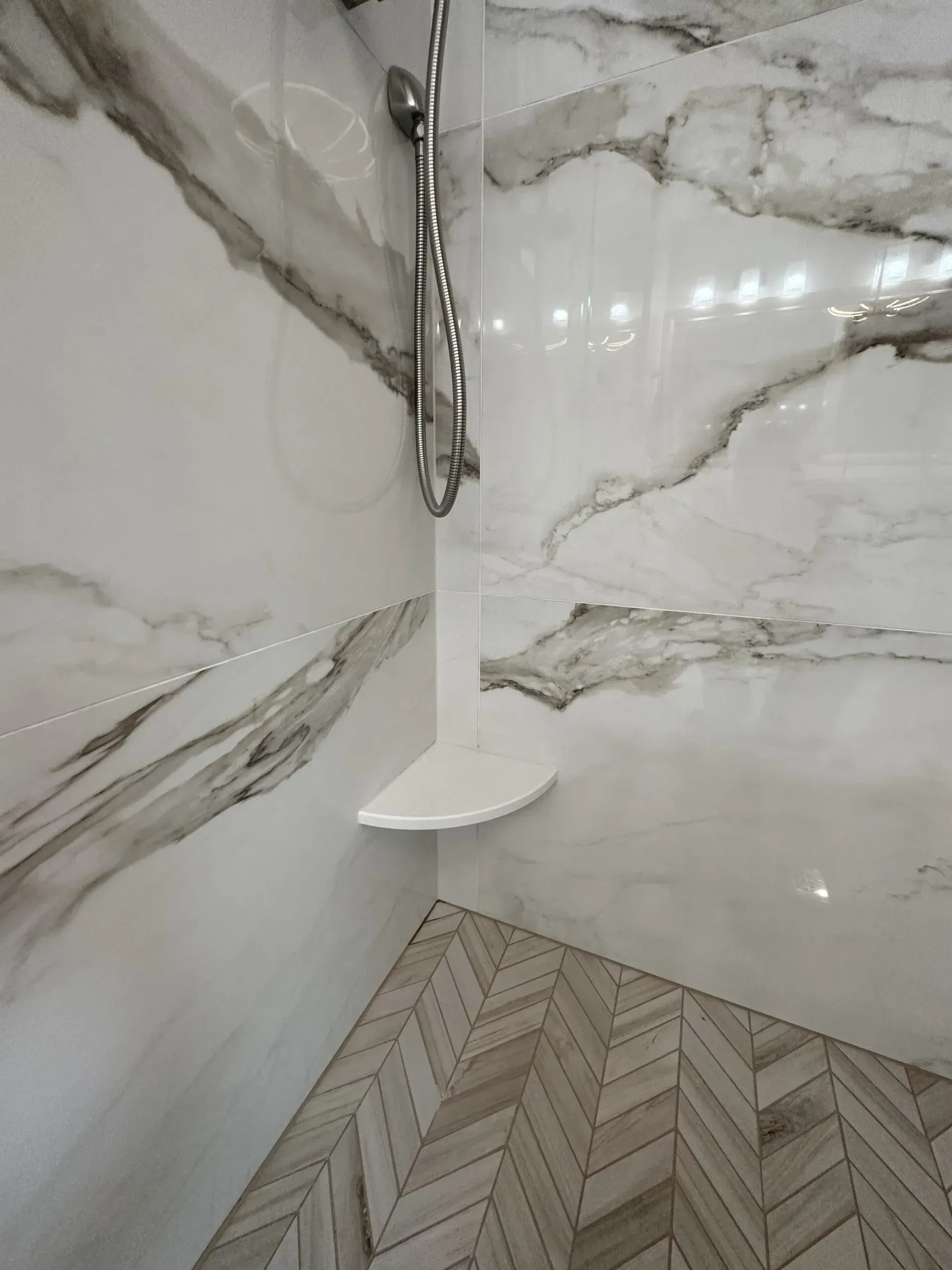Modern shower stall with marble-look tile walls, herringbone floor, and handheld showerhead