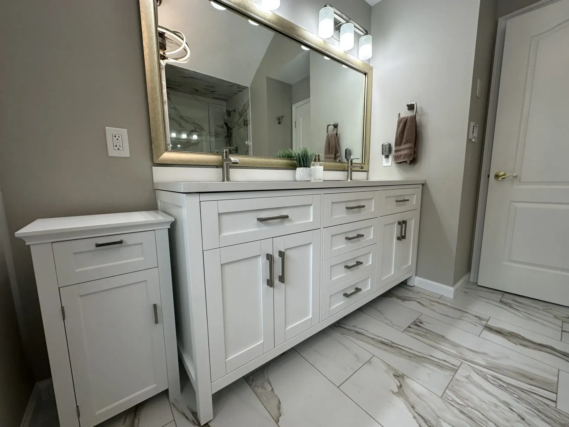 White bathroom vanity with double sink, large mirror, and tiled floor under warm lights