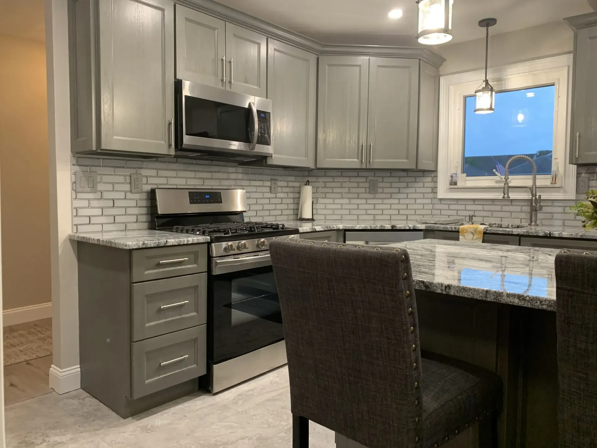Modern gray kitchen with stainless appliances, marble island, white tile backsplash, and pendant lights