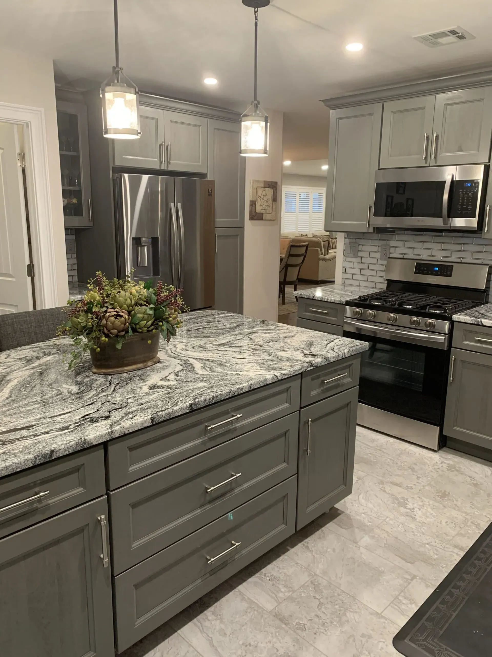 Modern kitchen with gray island, granite counters, stainless steel appliances, and pendant lights