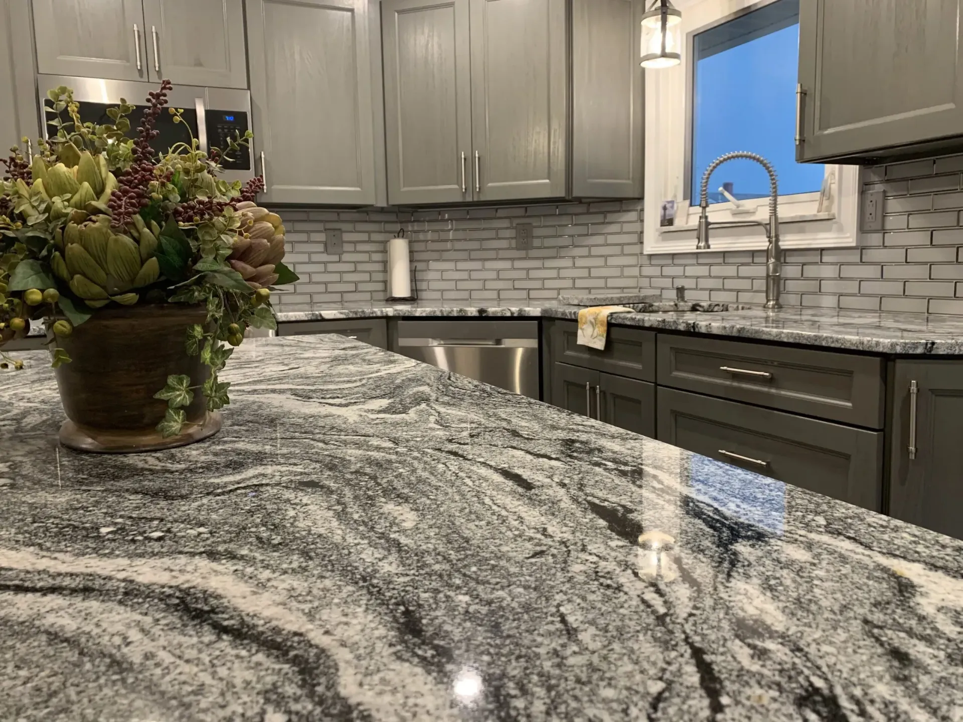 Modern kitchen with gray cabinets, white backsplash, granite countertop, and a floral arrangement on the island