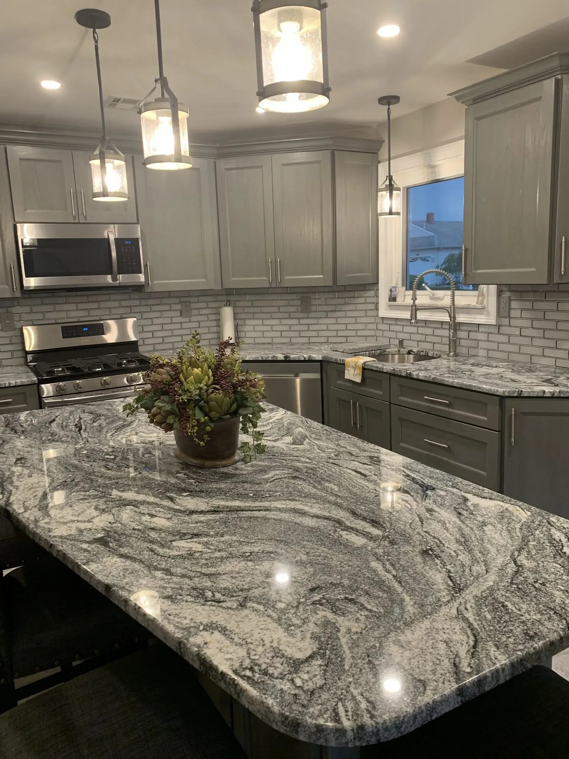 Modern kitchen with gray cabinets, granite island, pendant lights, and stainless steel appliances