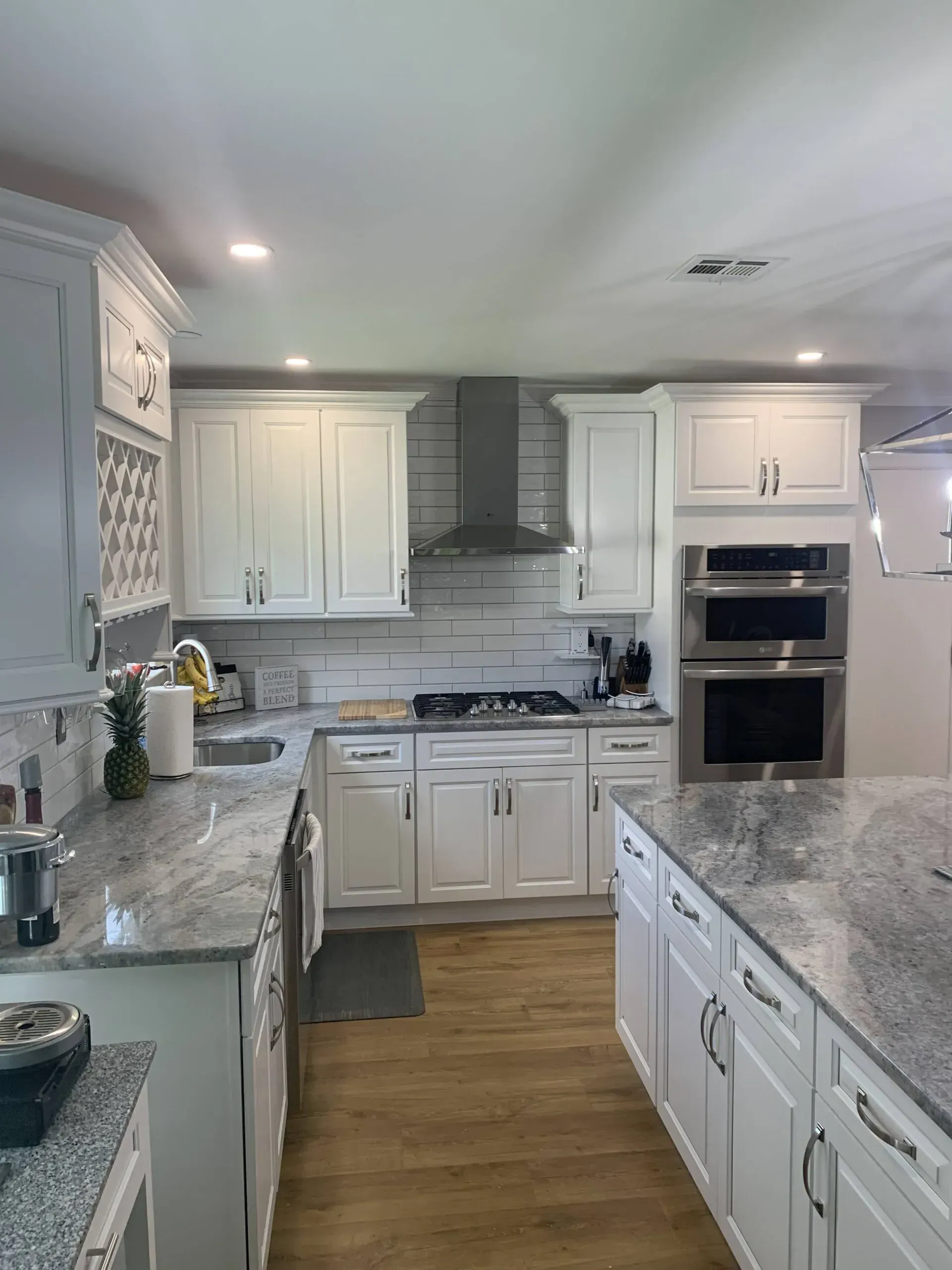 Bright white kitchen with gray countertops, wood floor, and stainless steel oven and range hood.