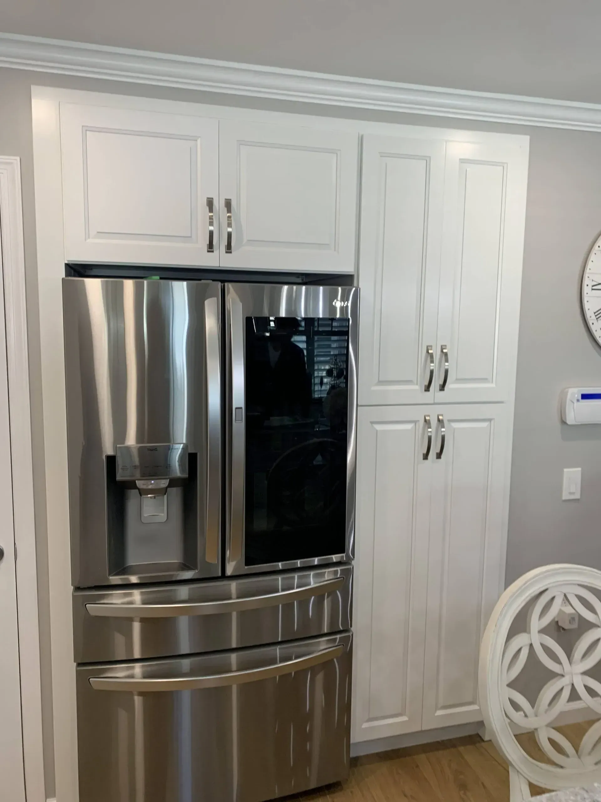 Stainless steel refrigerator beside white pantry cabinets in a bright kitchen