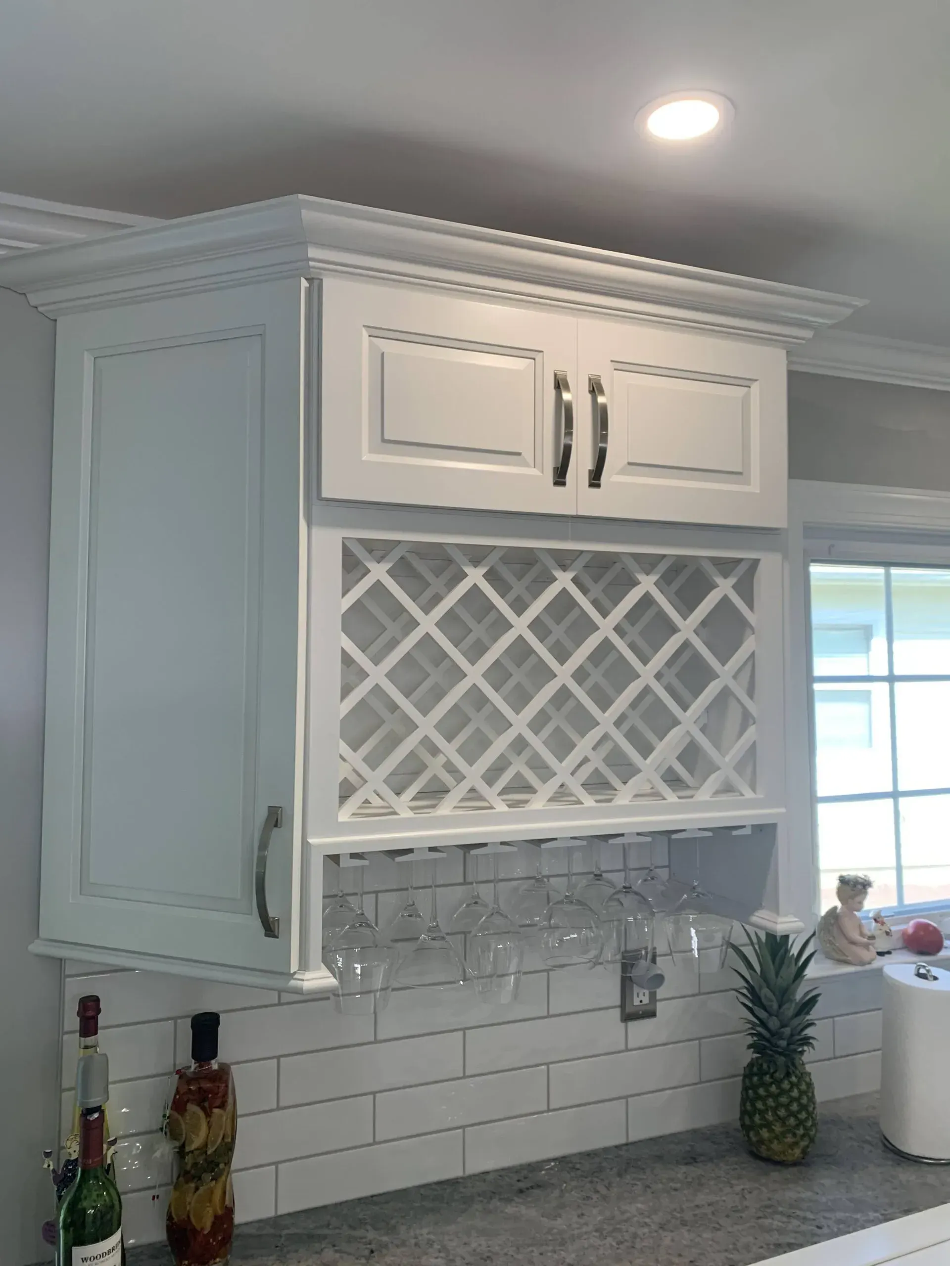 White kitchen cabinet with a wine rack and recessed lighting above a white subway tile backsplash