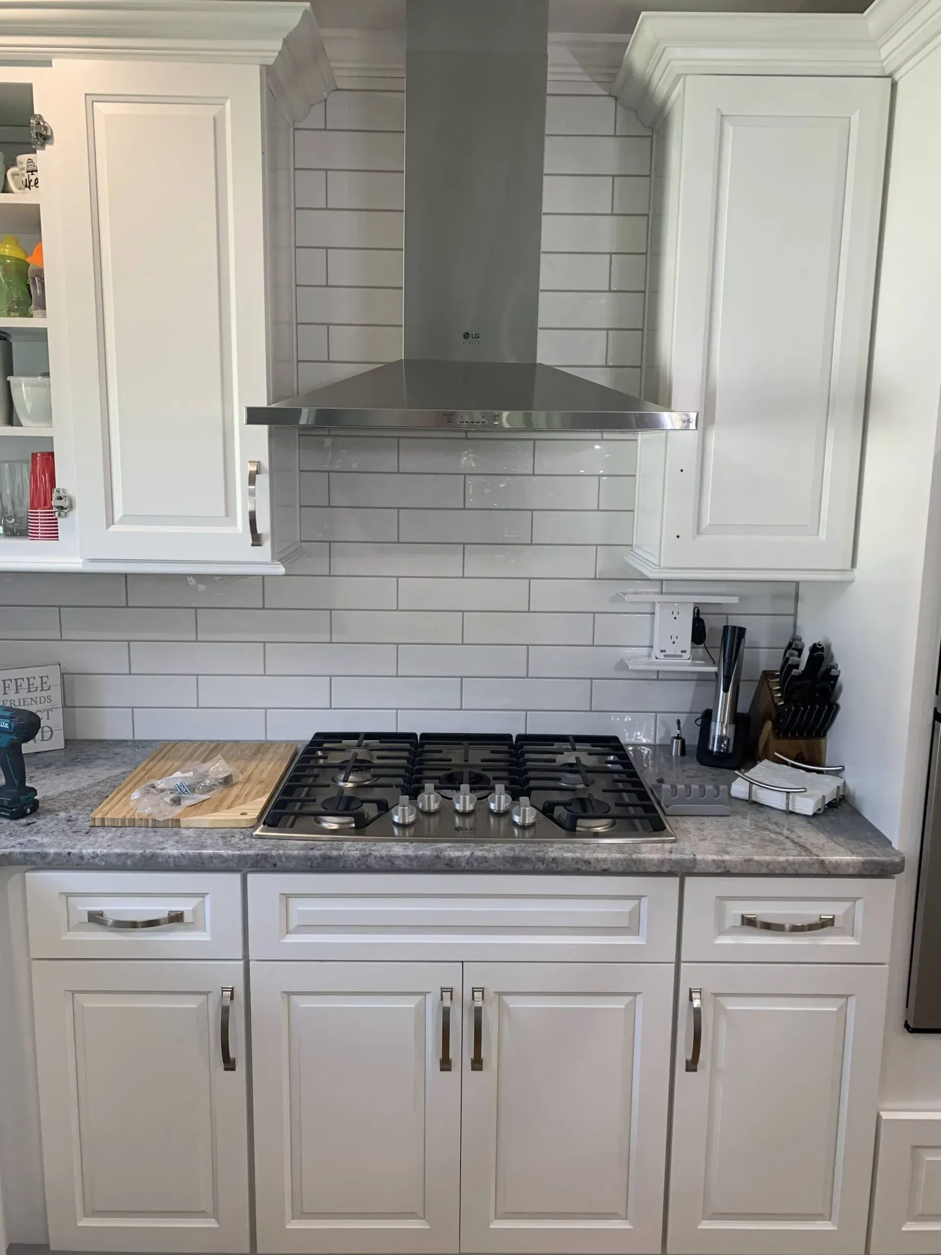 Modern kitchen with white cabinets, gray subway tile backsplash, gas cooktop, and stainless steel range hood