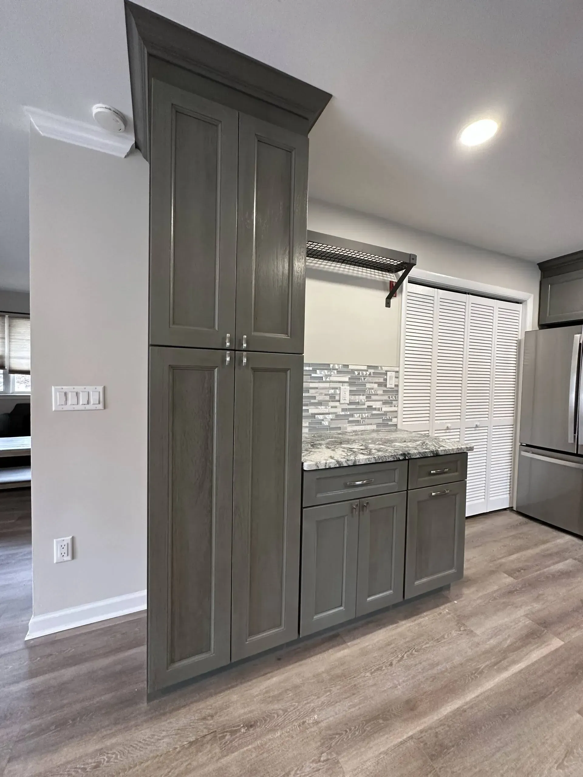 Kitchen nook with tall olive-green cabinets, granite counter, mosaic backsplash, and wood flooring