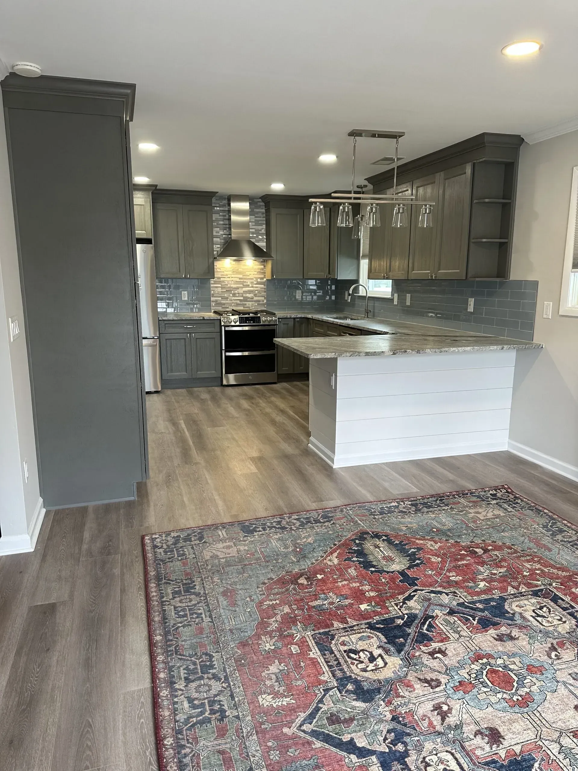 Empty modern kitchen and living area with gray cabinets, white island, and large patterned rug.