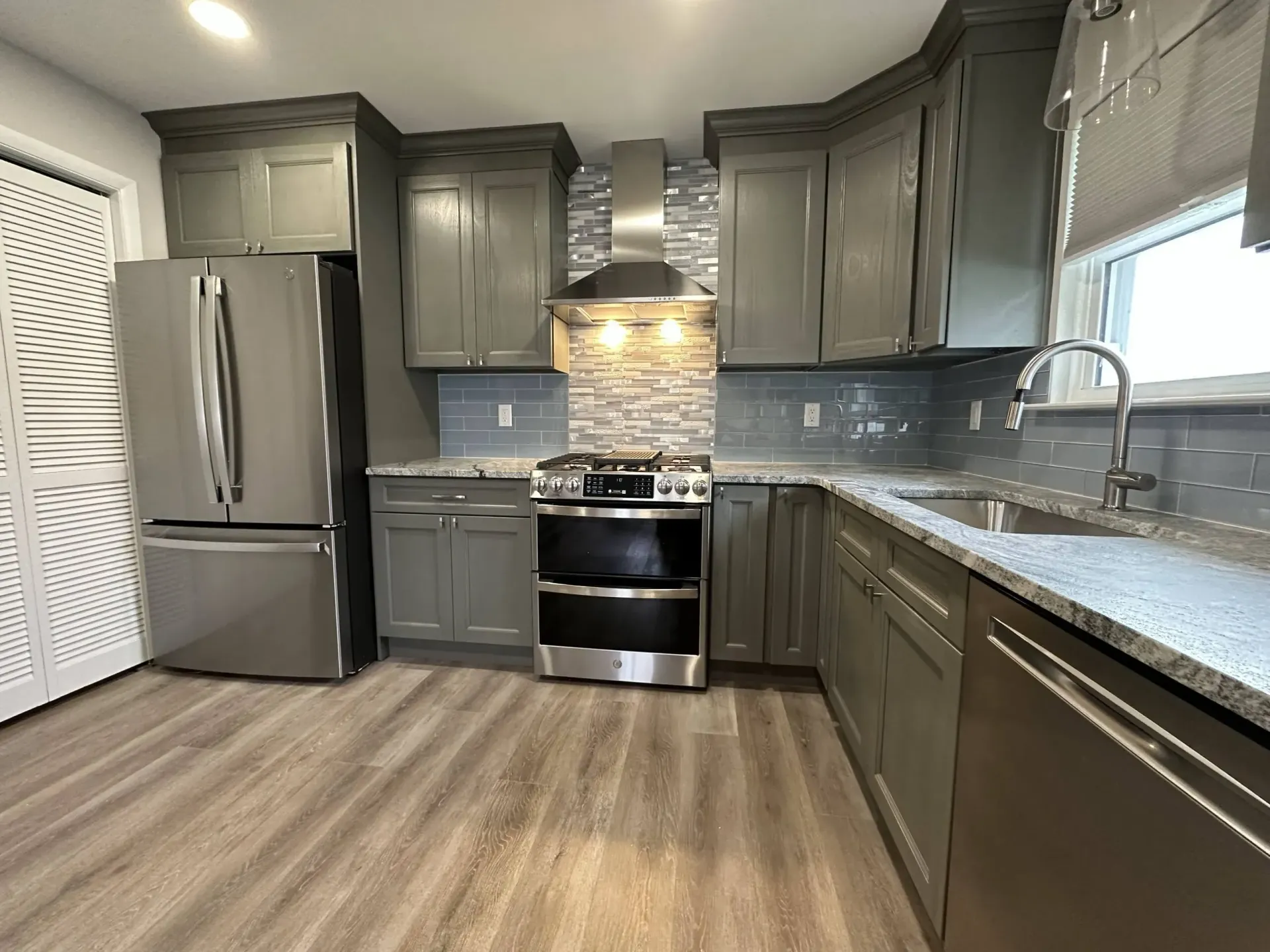 Modern kitchen with gray cabinets, stainless steel appliances, granite countertops, and wood-look flooring.