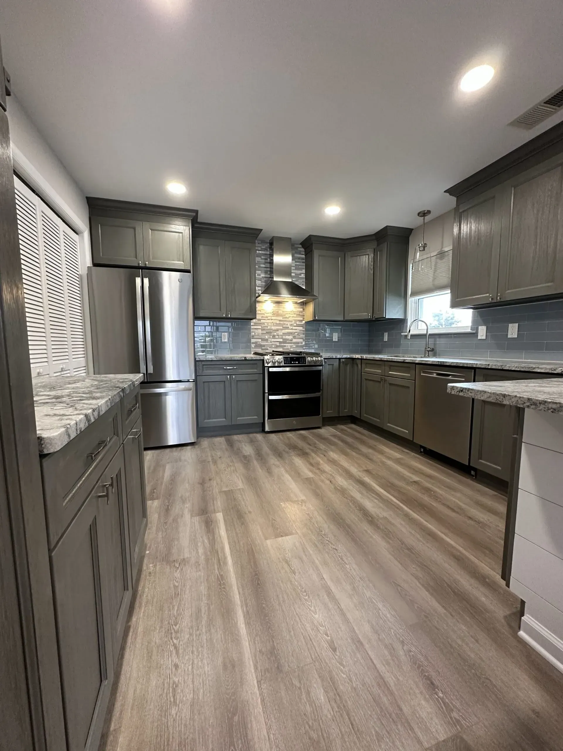 Modern gray kitchen with stainless steel appliances, wood floors, and granite countertops