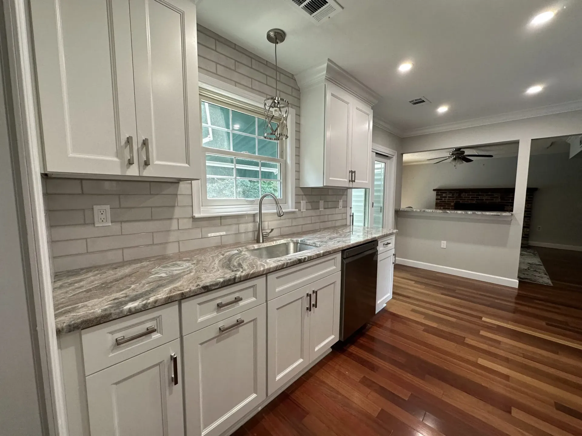 Bright white kitchen with granite counters, subway tile backsplash, stainless oven, and hardwood floors