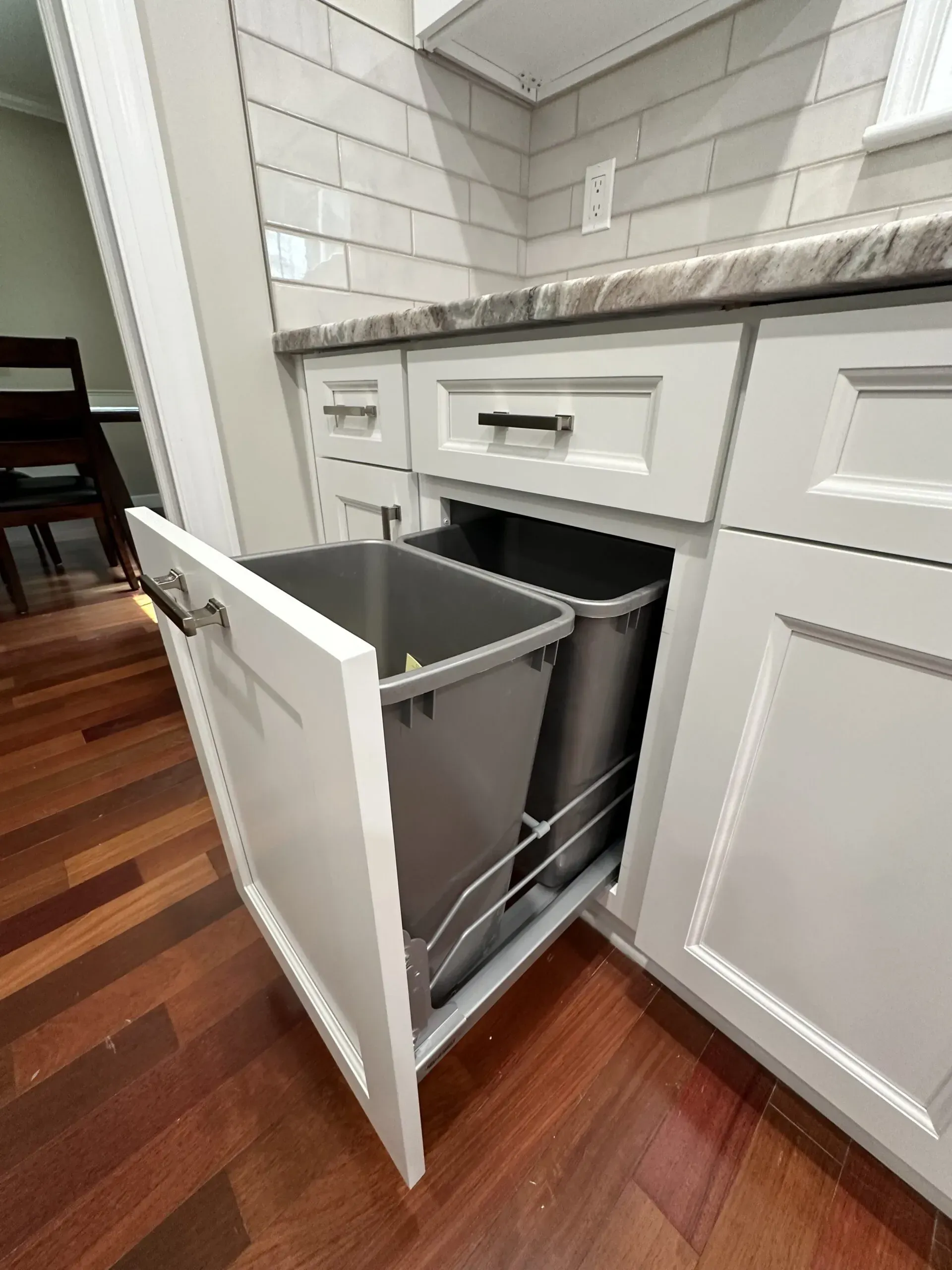 Open kitchen cabinet with pull-out trash and recycling bins under a countertop.