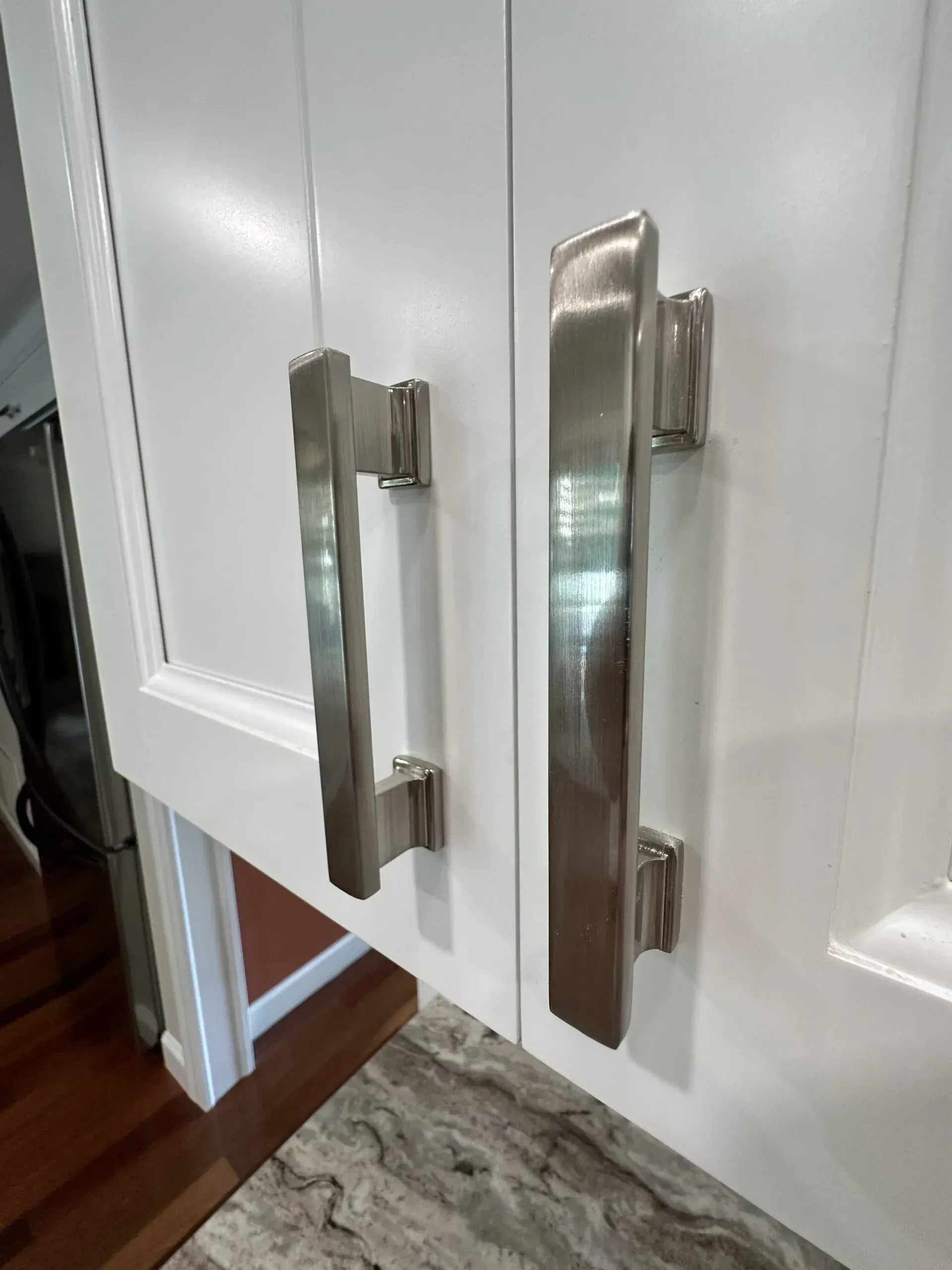 White cabinet doors with long brushed metal handles and a small floor vent nearby.