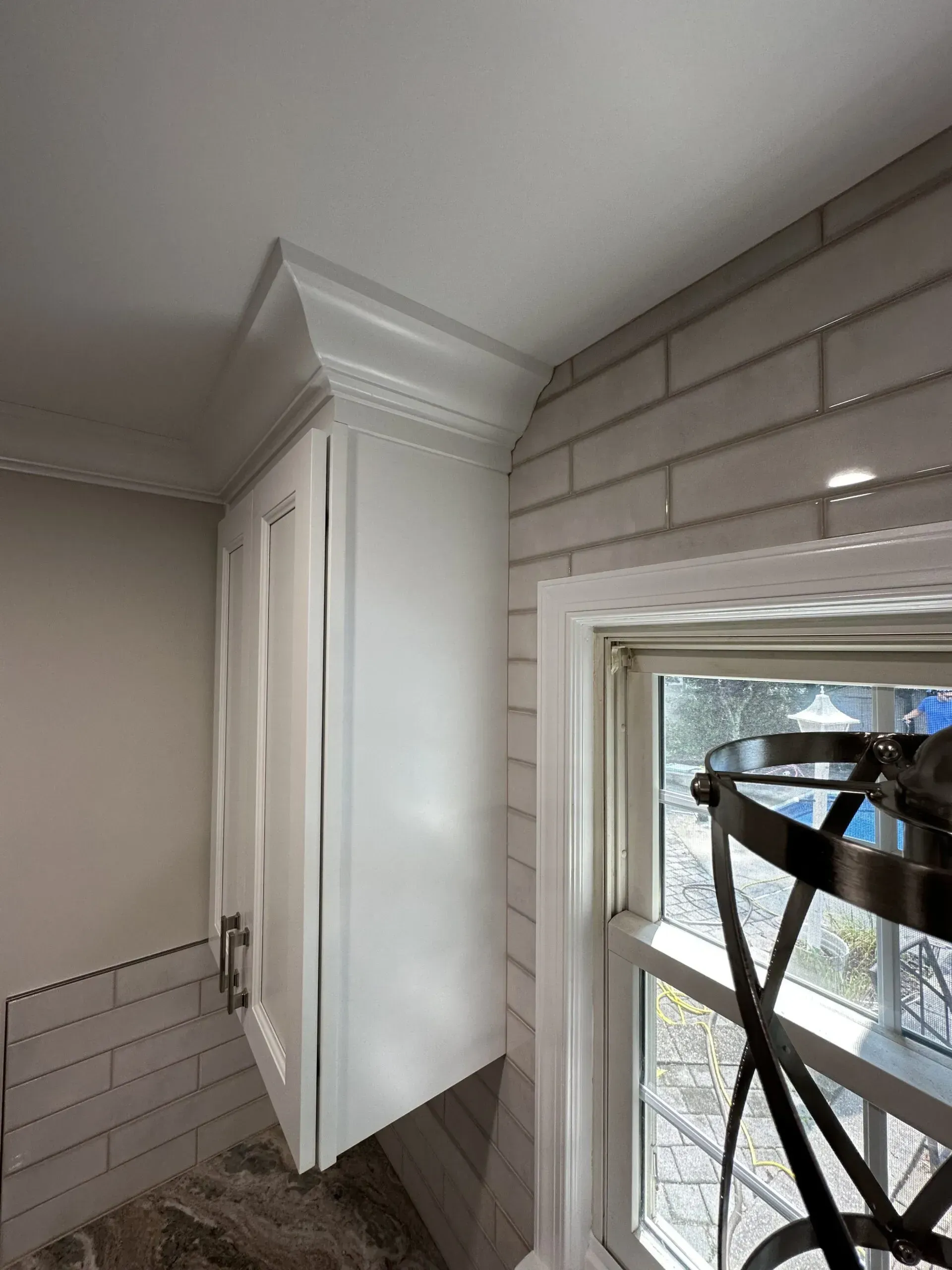 White kitchen corner with tiled walls, cabinet, and a window partly covered with tape.