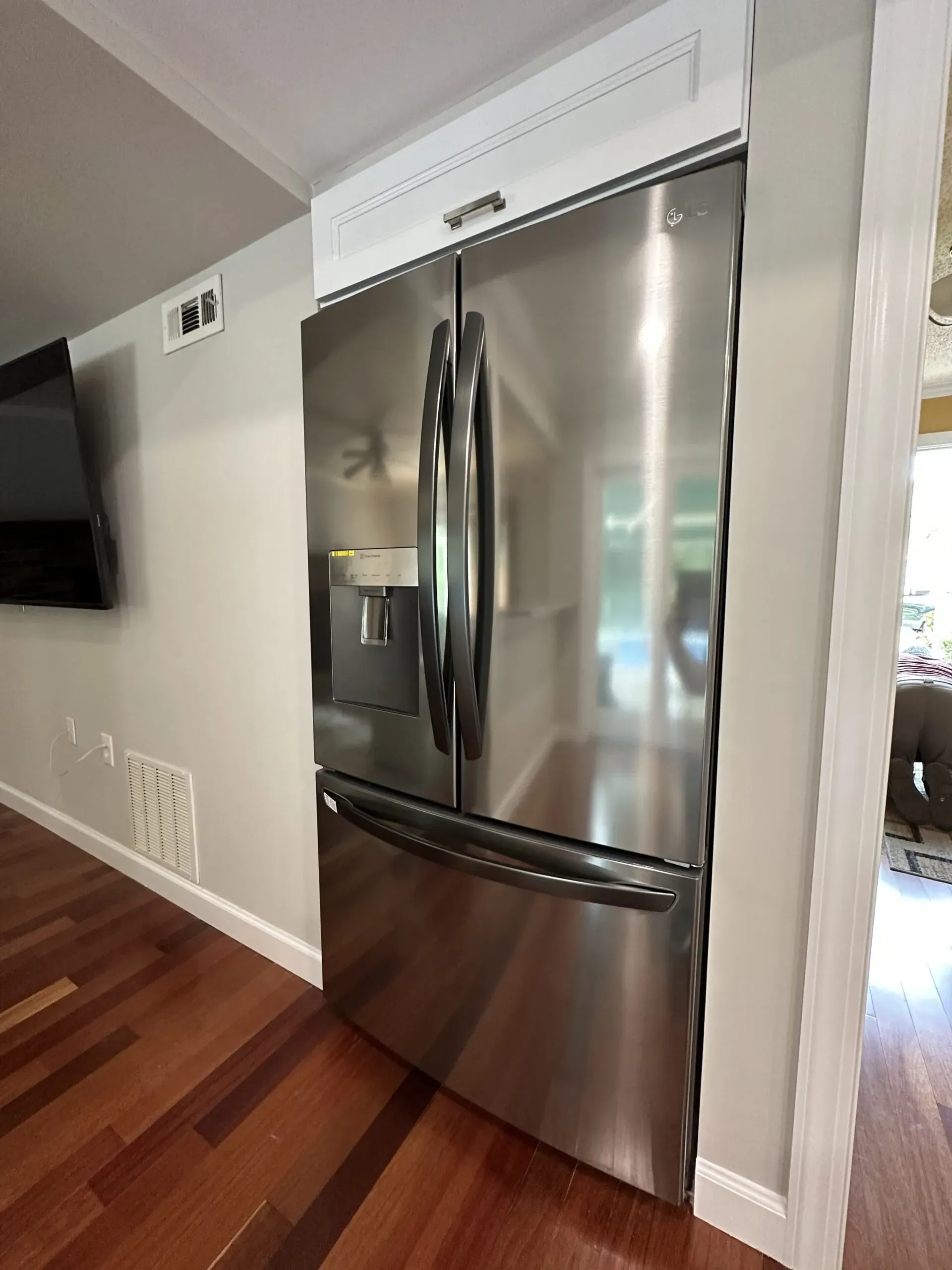 Stainless steel French-door refrigerator in a modern kitchen with hardwood floors and white walls
