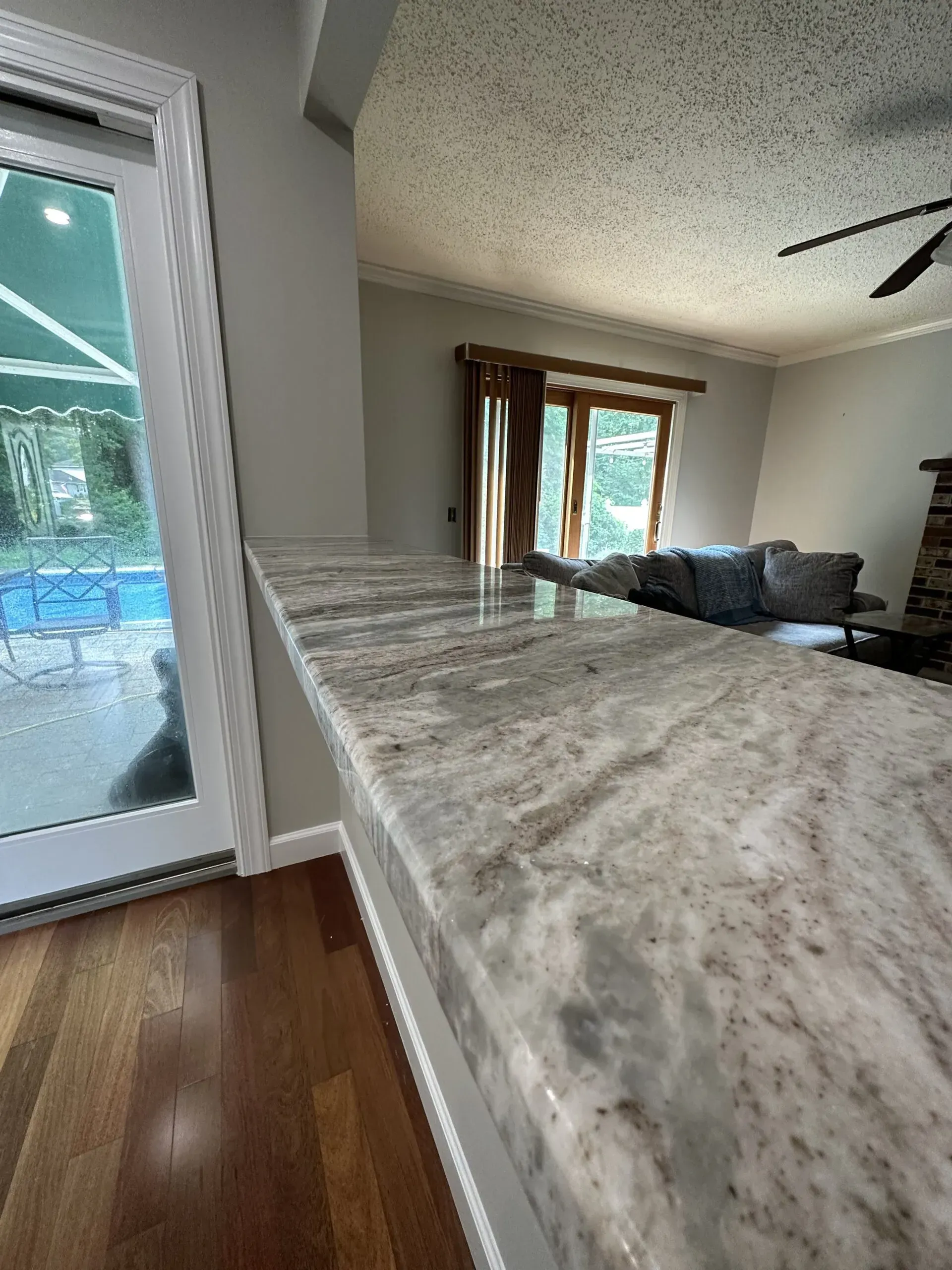 Sunlit living room with marble kitchen counter, hardwood floor, and sliding glass door to a patio