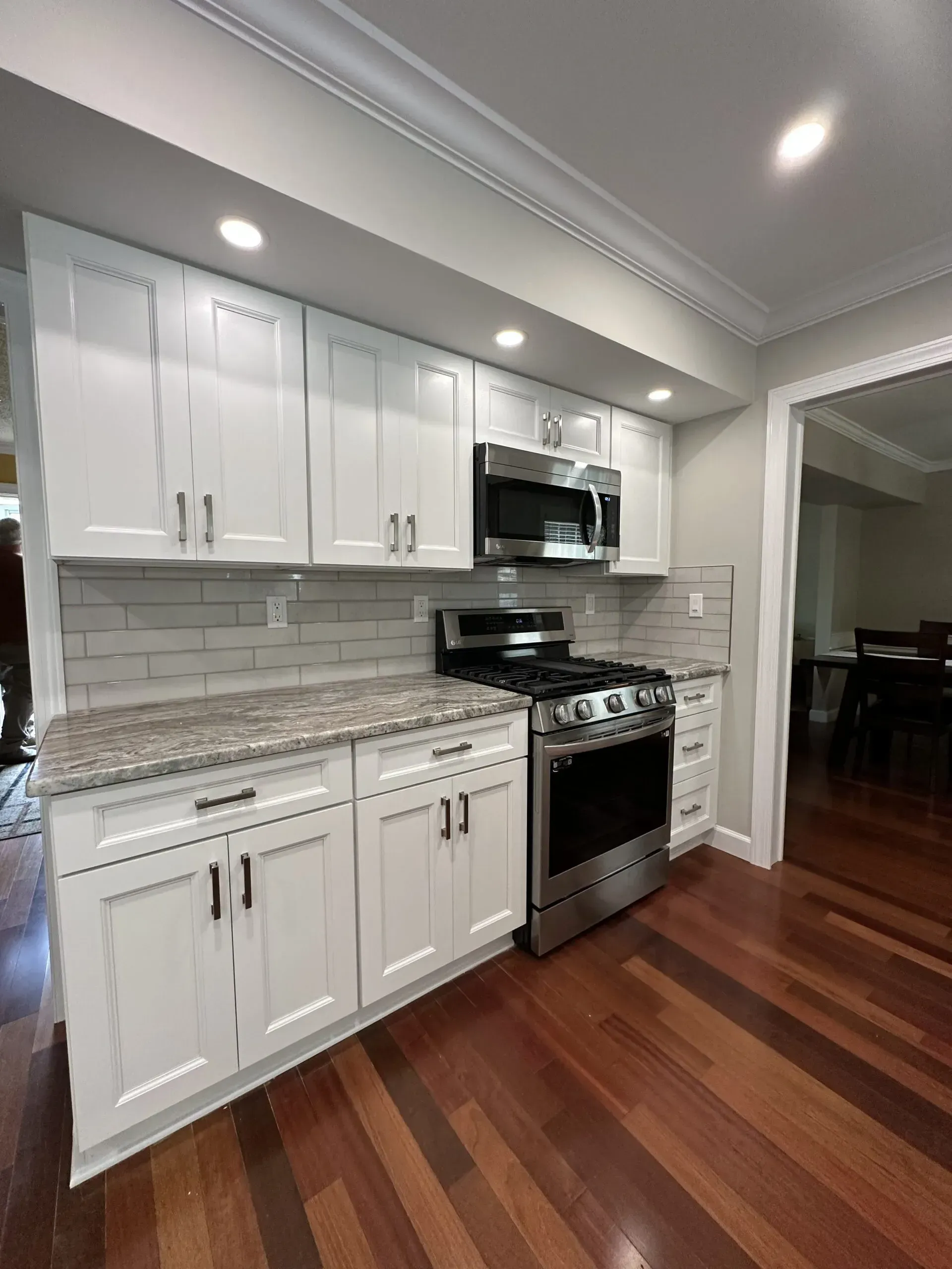 Bright kitchen with white cabinets, gray tile backsplash, stainless stove, and hardwood floors
