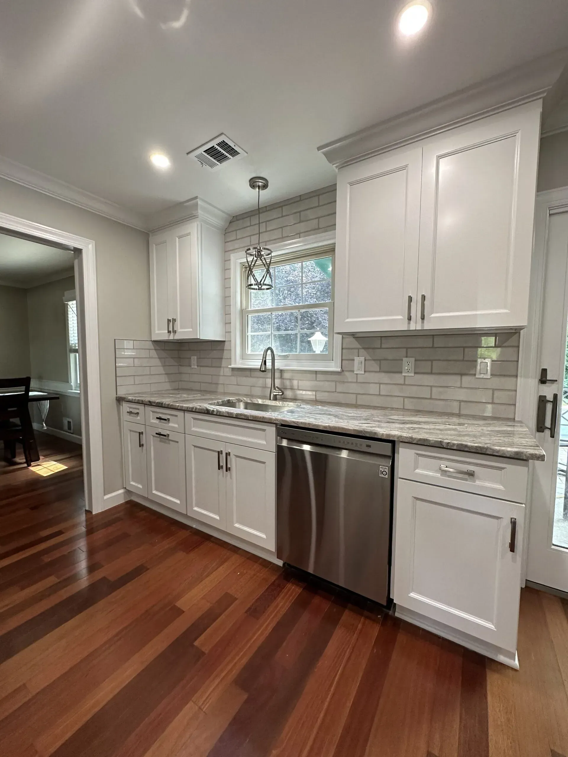 Modern white kitchen with stainless steel appliances, marble backsplash, and hardwood floors