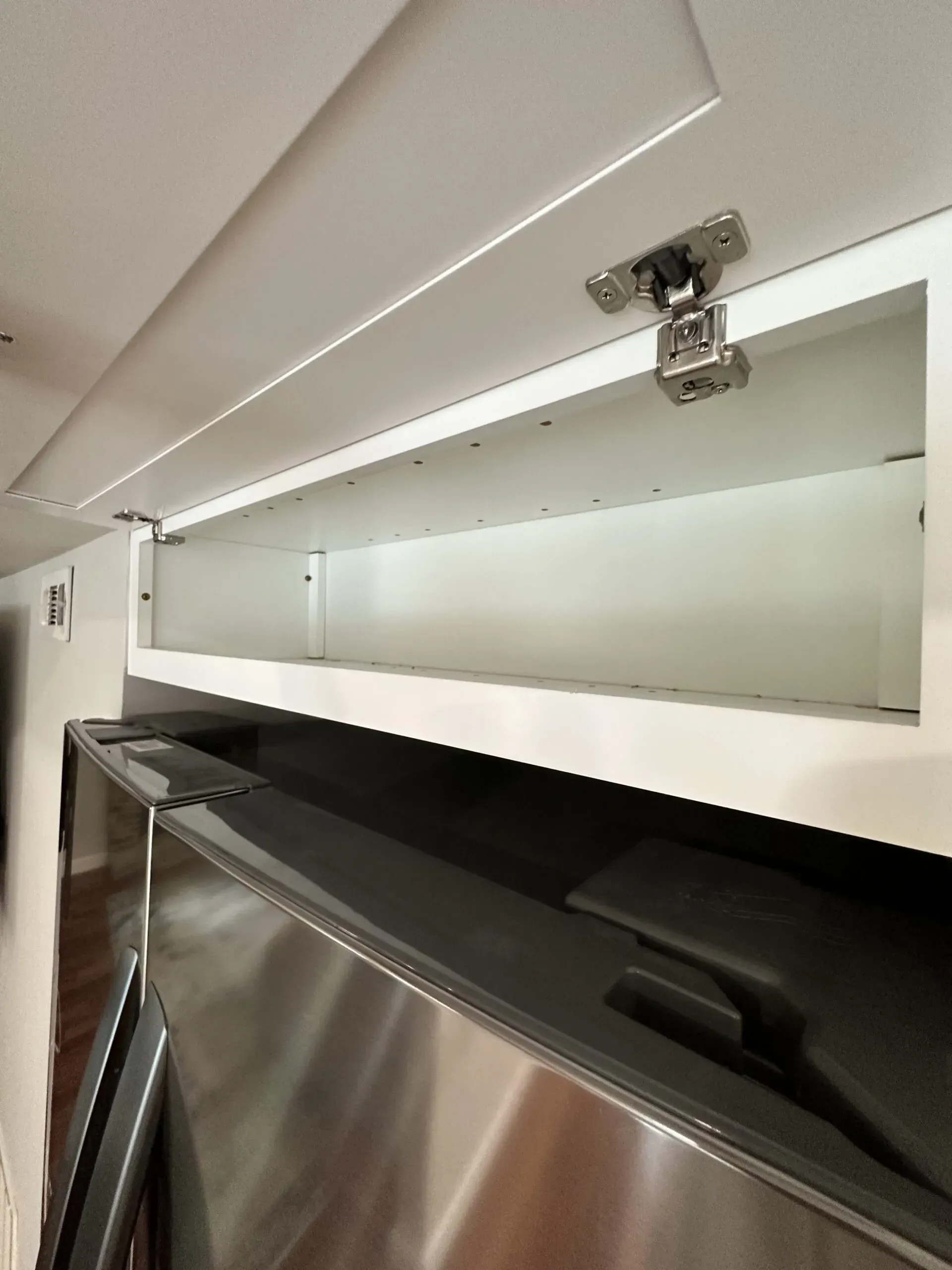 Open storage compartment with white lid, metal hinge, and black interior above a stainless steel panel.