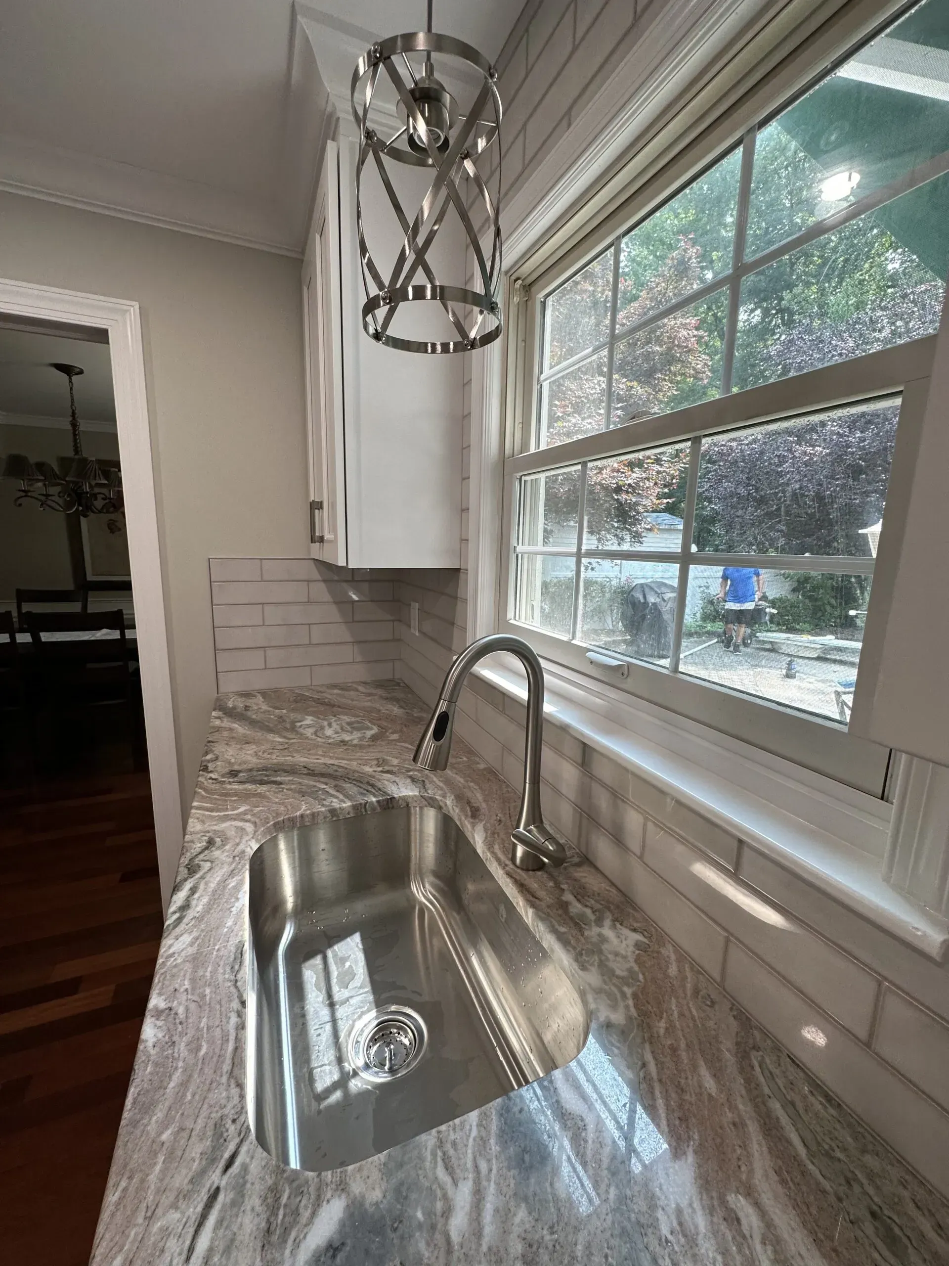 Bright kitchen with a stainless-steel sink, marble countertop, subway tile backsplash, and large window.