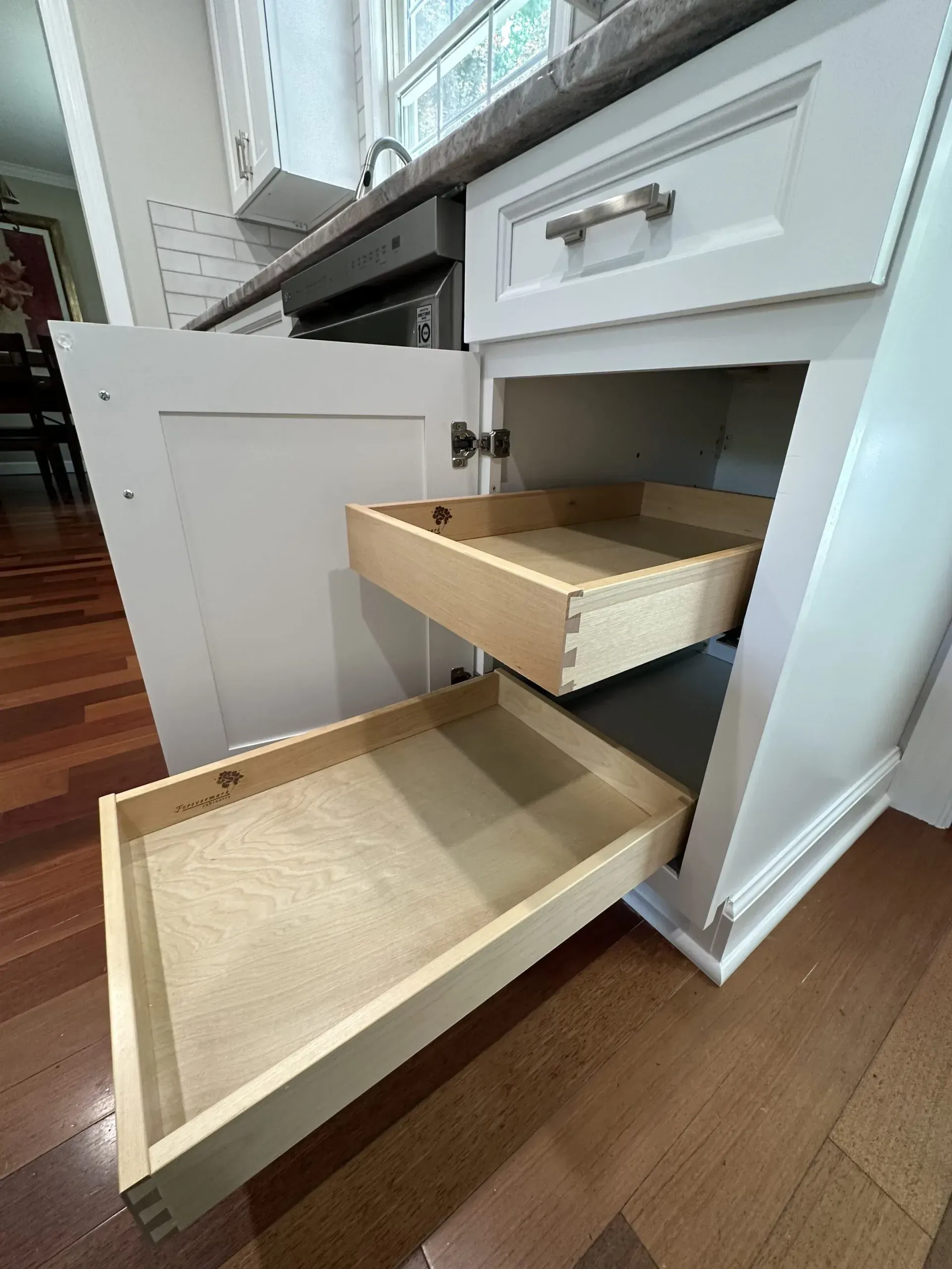 Open drawers in a white kitchen cabinet, showing shallow wooden drawer boxes and a pull-out tray.