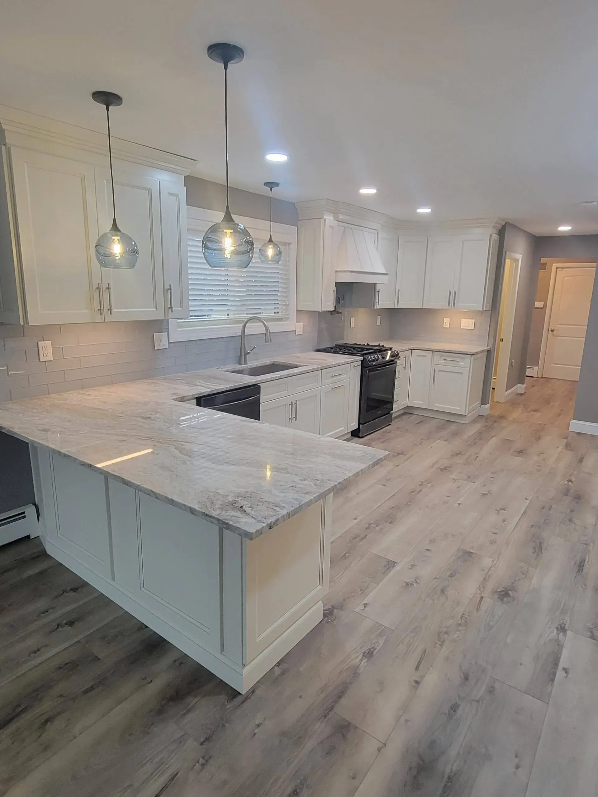 Bright modern kitchen with white cabinets, marble island, pendant lights, and gray wood flooring