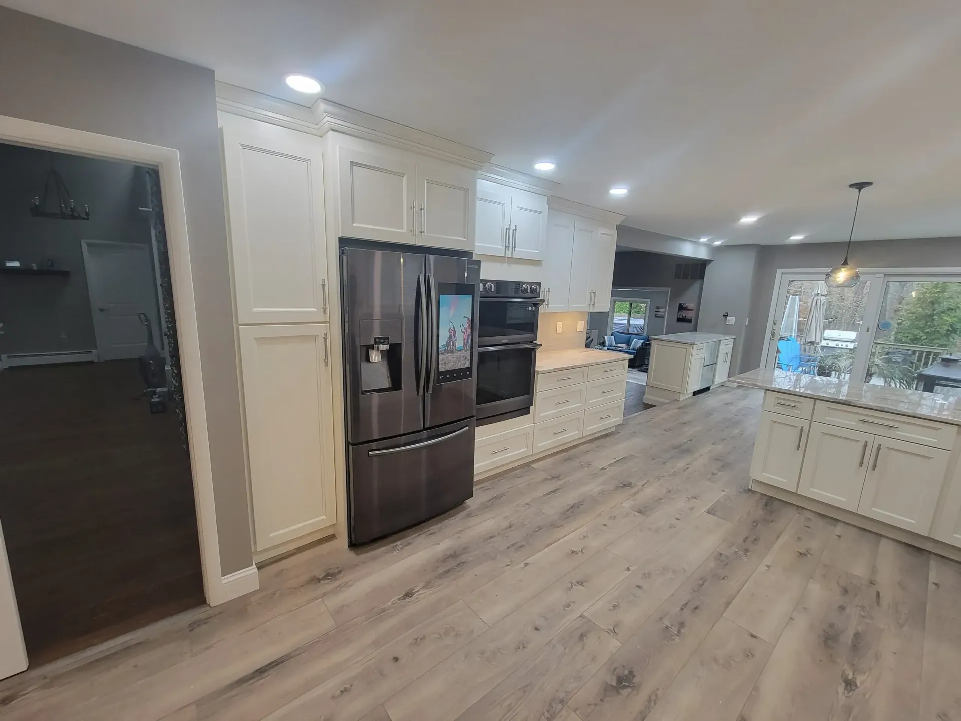 Bright modern kitchen with white cabinets, stainless fridge, island, and wood-look flooring