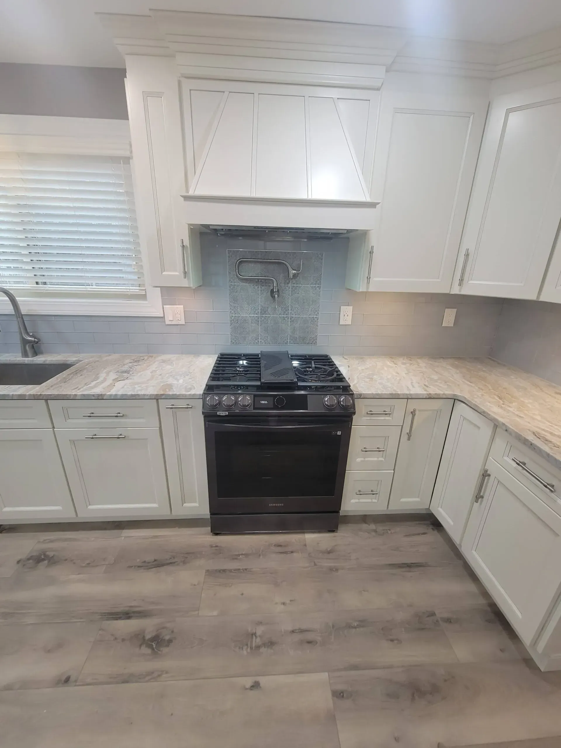 White kitchen with black stove, light countertops, white cabinets, and wood-look flooring