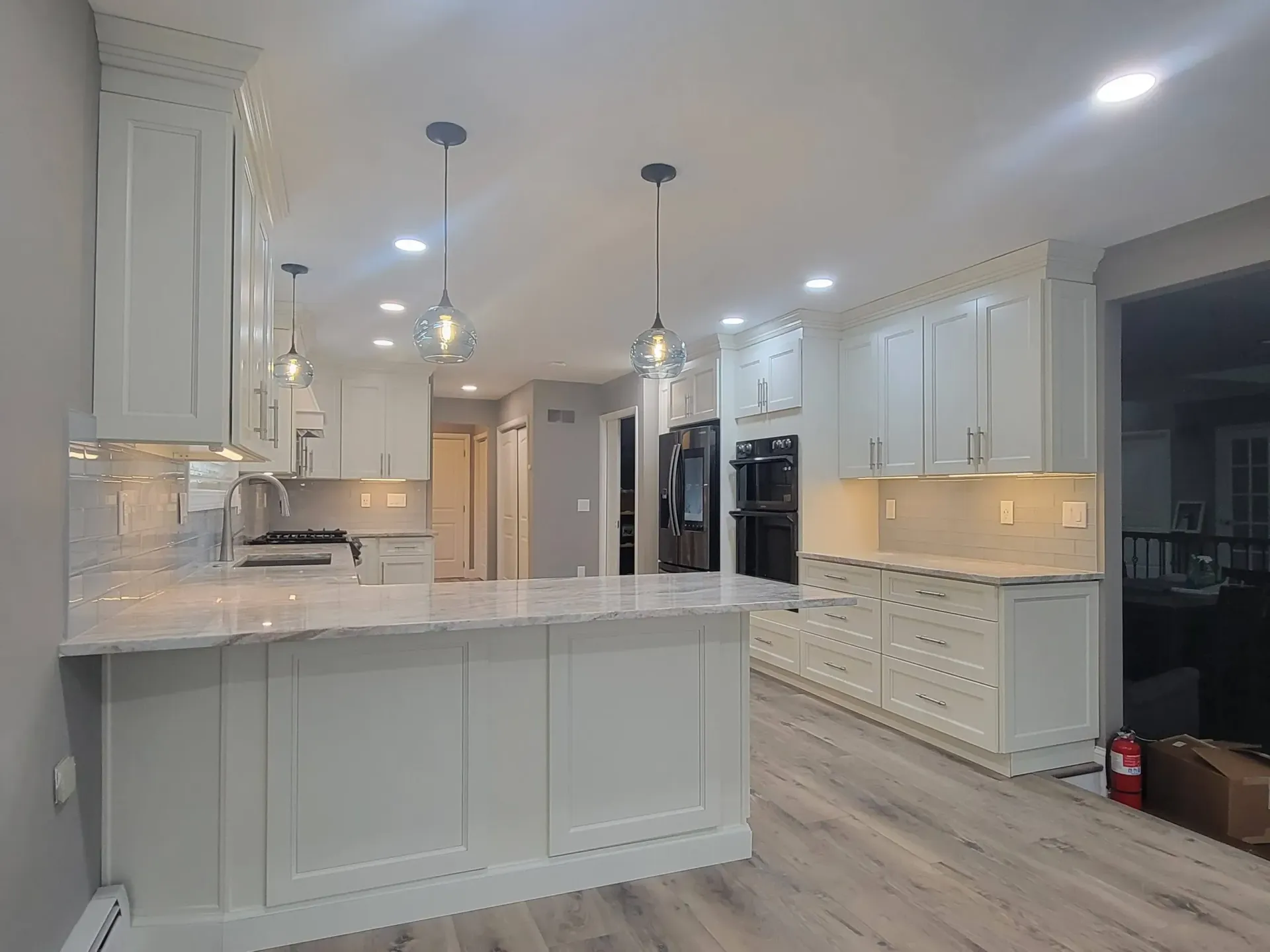 Bright white modern kitchen with island, pendant lights, recessed lighting, and black appliances