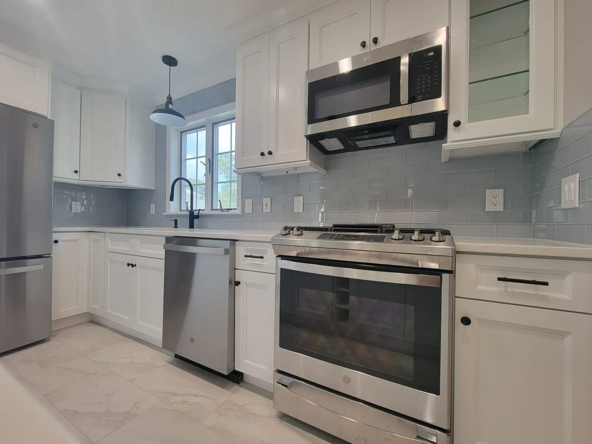 Bright modern kitchen with white cabinets, stainless steel appliances, and light tile flooring