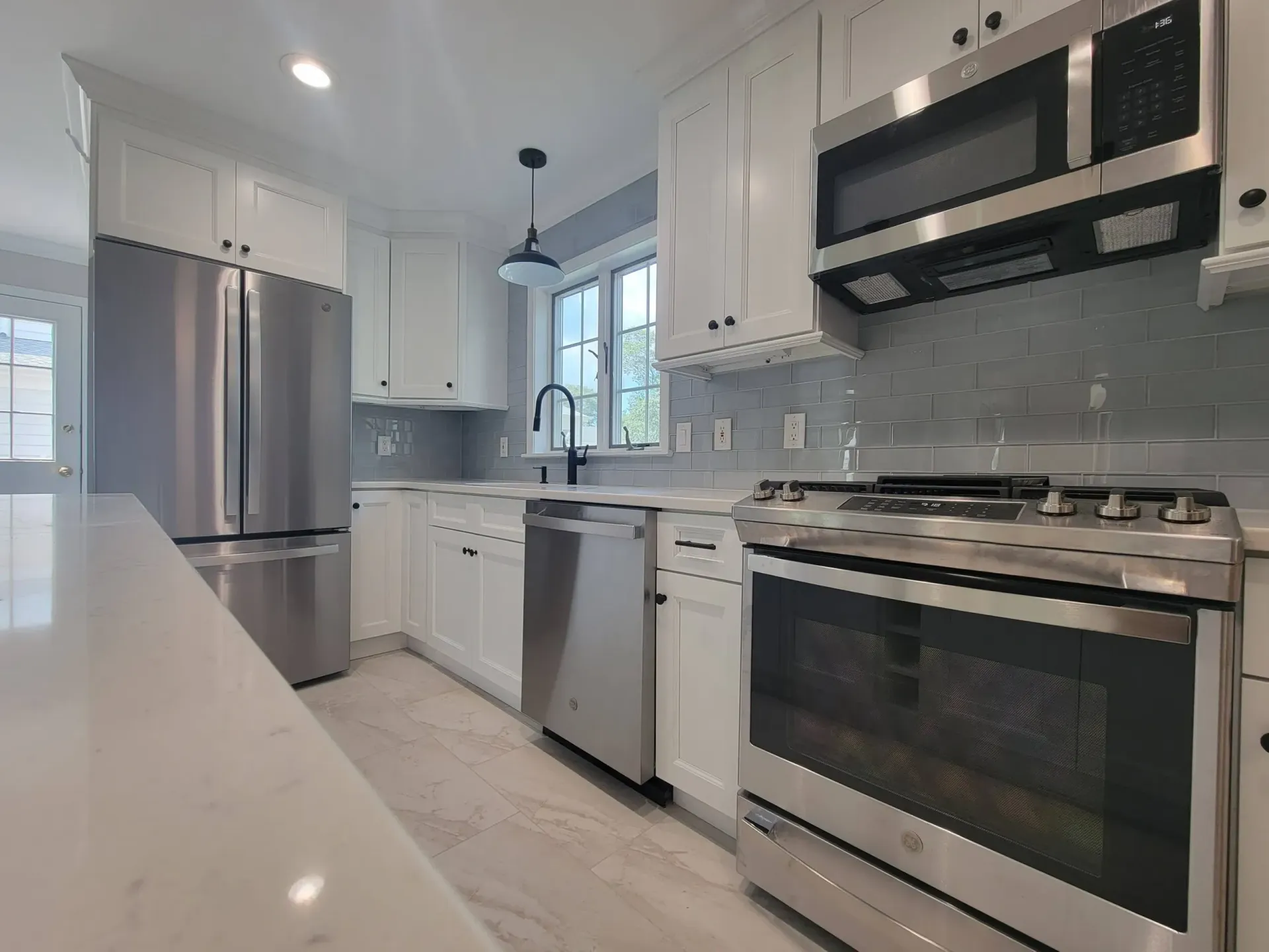 Modern white kitchen with stainless steel appliances, tiled backsplash, and a window over the sink