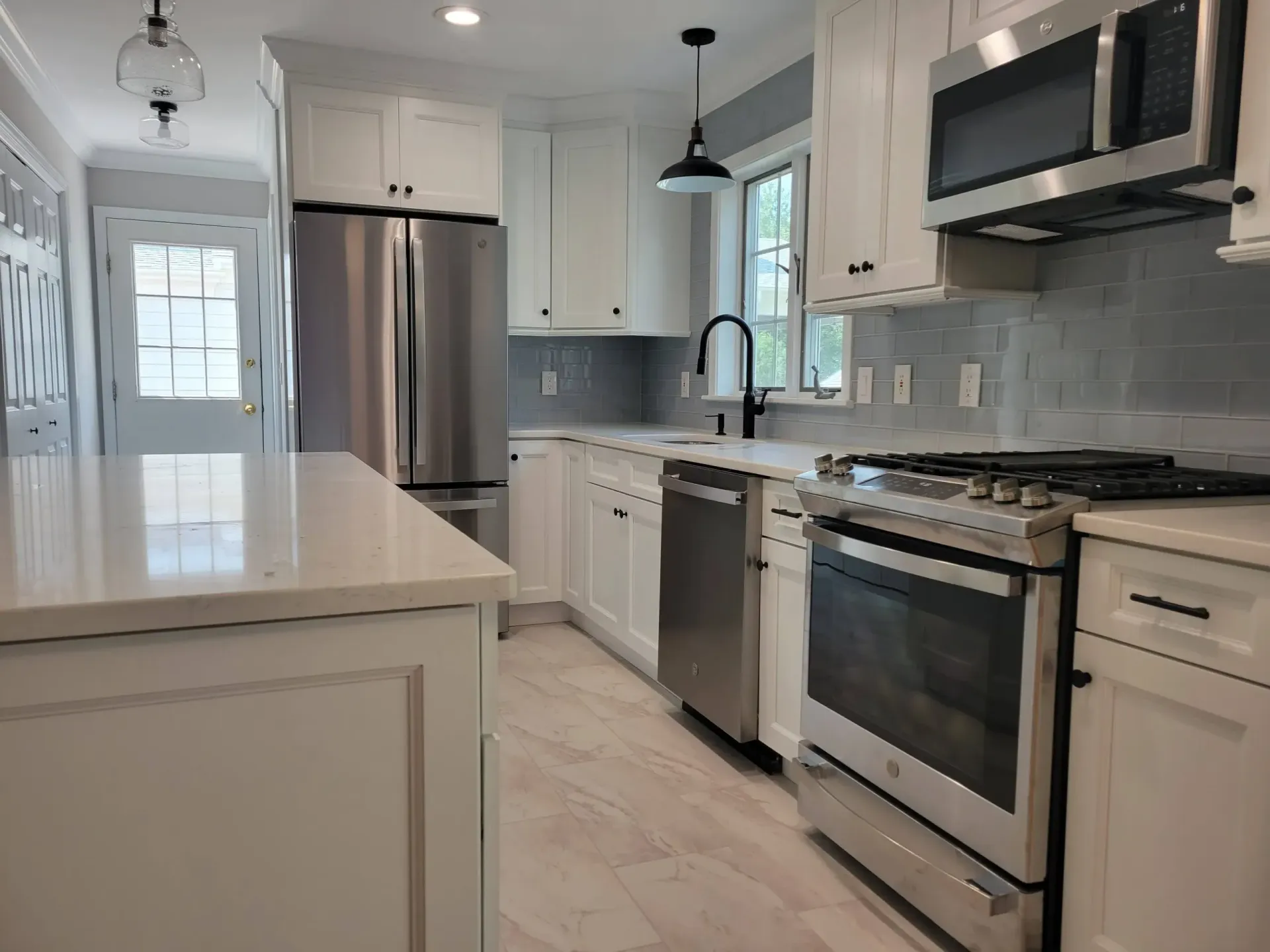 Bright modern kitchen with white cabinets, stainless steel appliances, island, and light tile floor