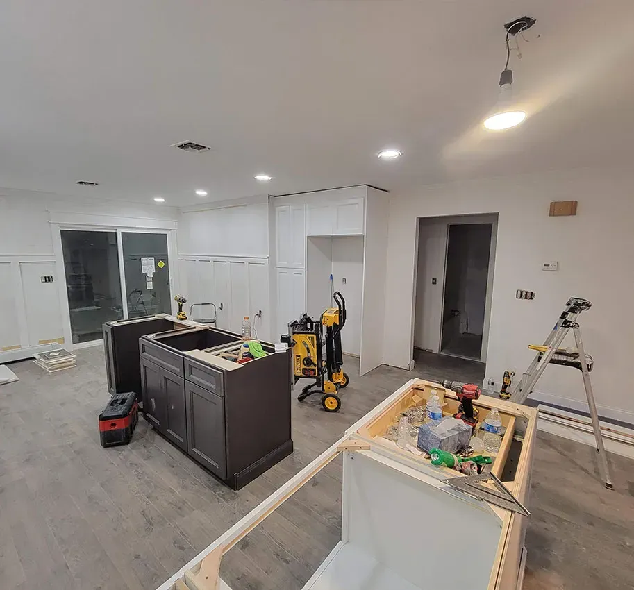 Unfinished kitchen with cabinets, tools, and construction supplies in a bright room